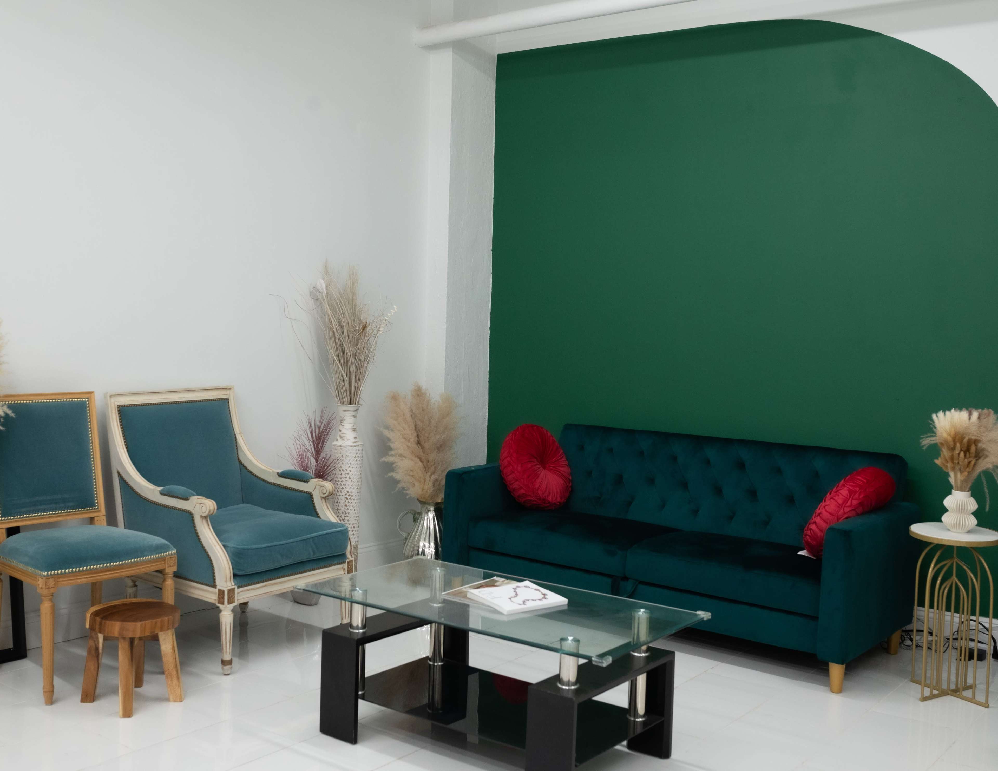 The image shows a modern living room with a green accent wall, a teal sofa with red pillows, a glass coffee table, and decorative plants.