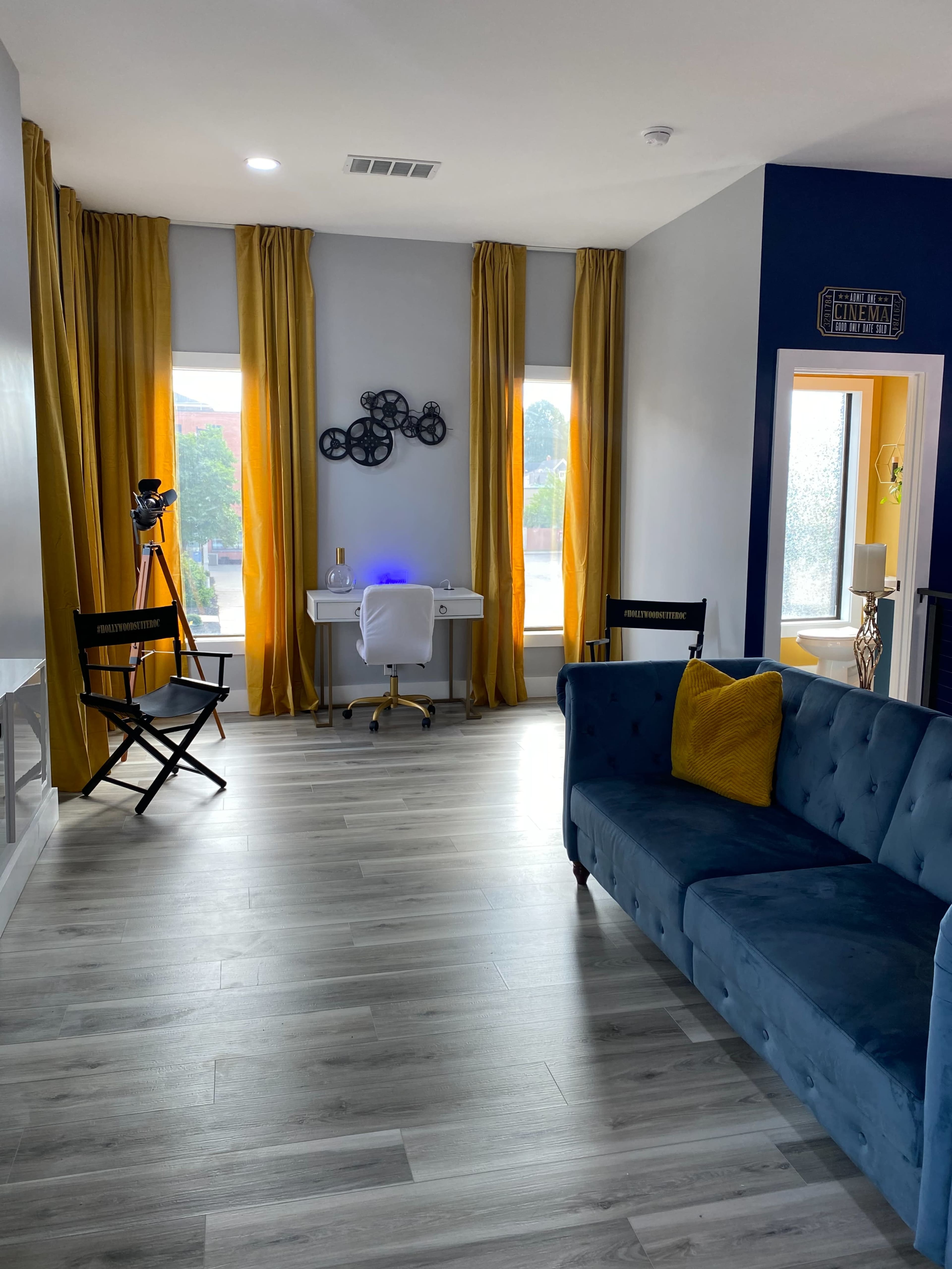 A bright, modern room with a blue couch, a white desk with a chair, and large yellow curtains.