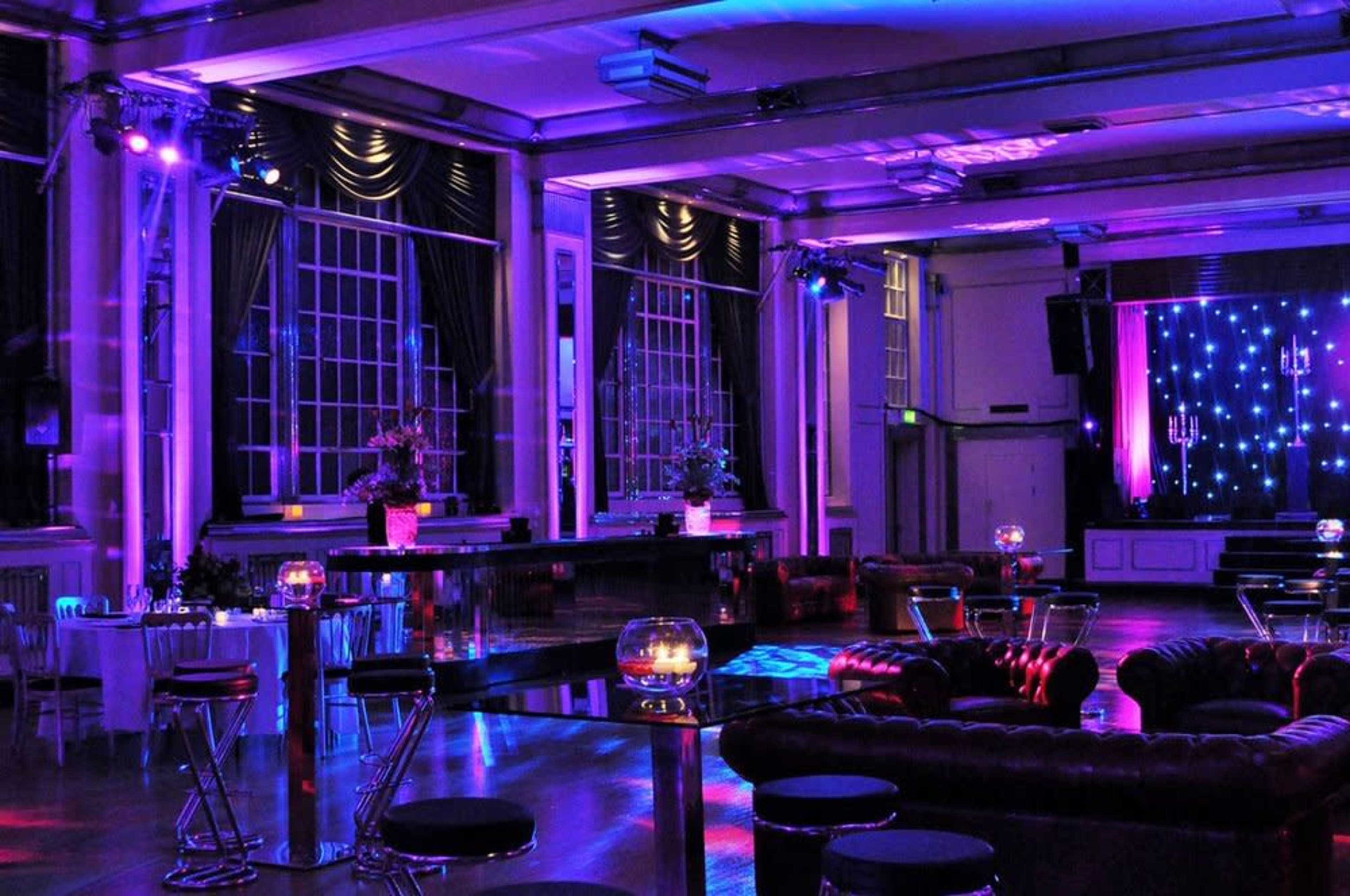 An elegantly decorated event space with colorful lighting, featuring lounge seating and tables set up for guests.