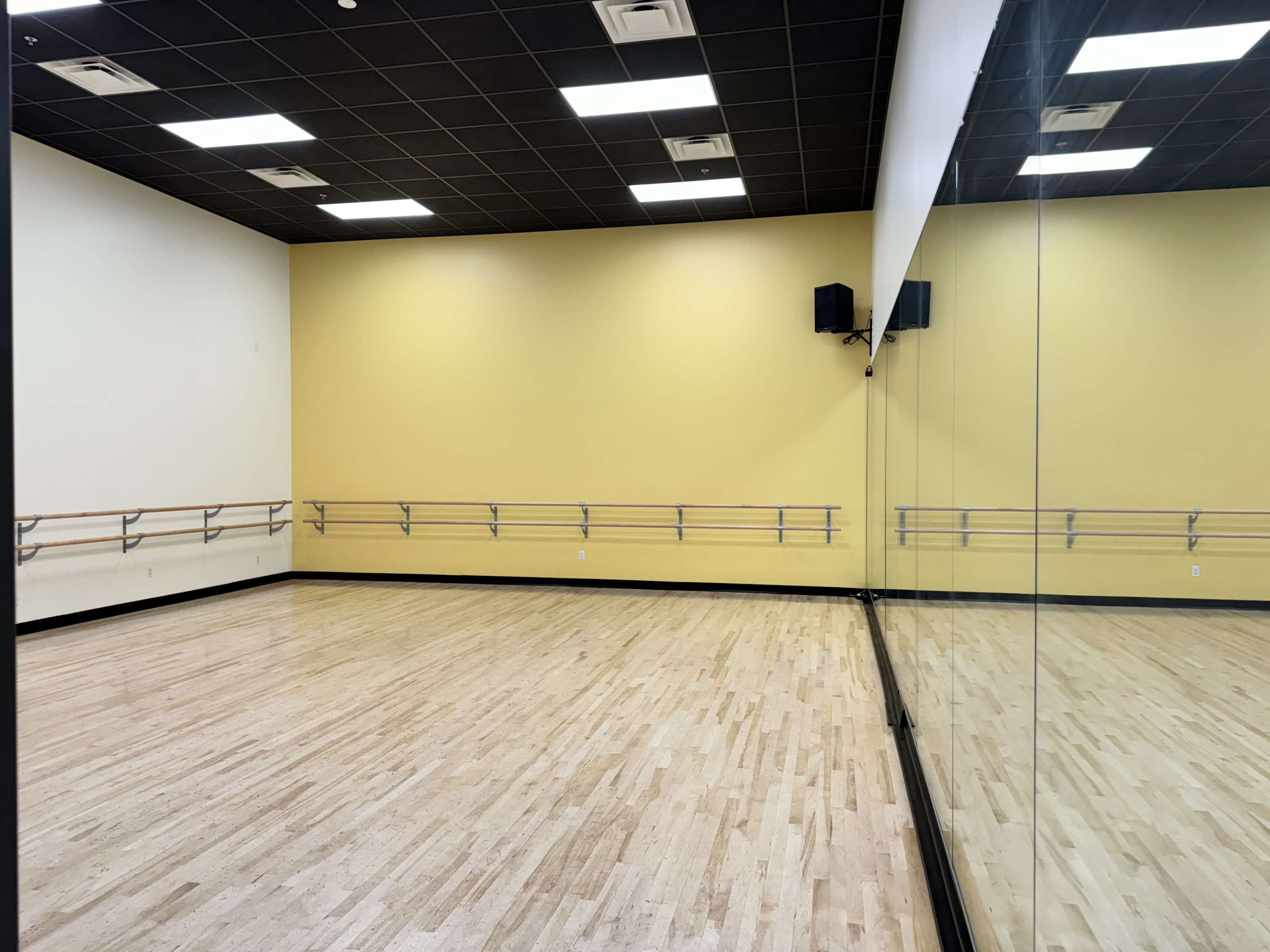 A spacious dance studio with wooden flooring, yellow walls, and a mirrored wall along one side.