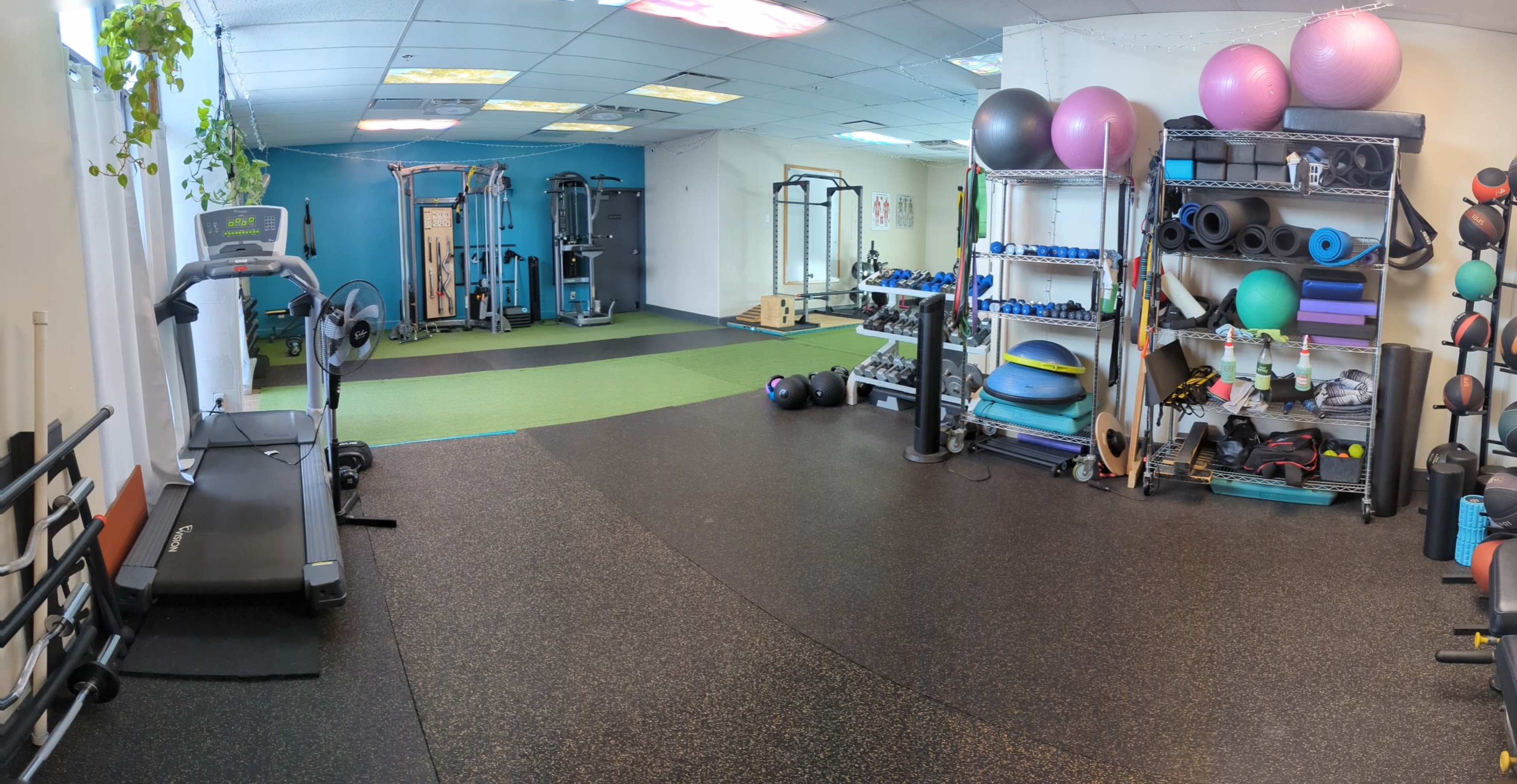 A gym interior with exercise equipment, including a treadmill, weights, and various fitness accessories arranged along the walls.
