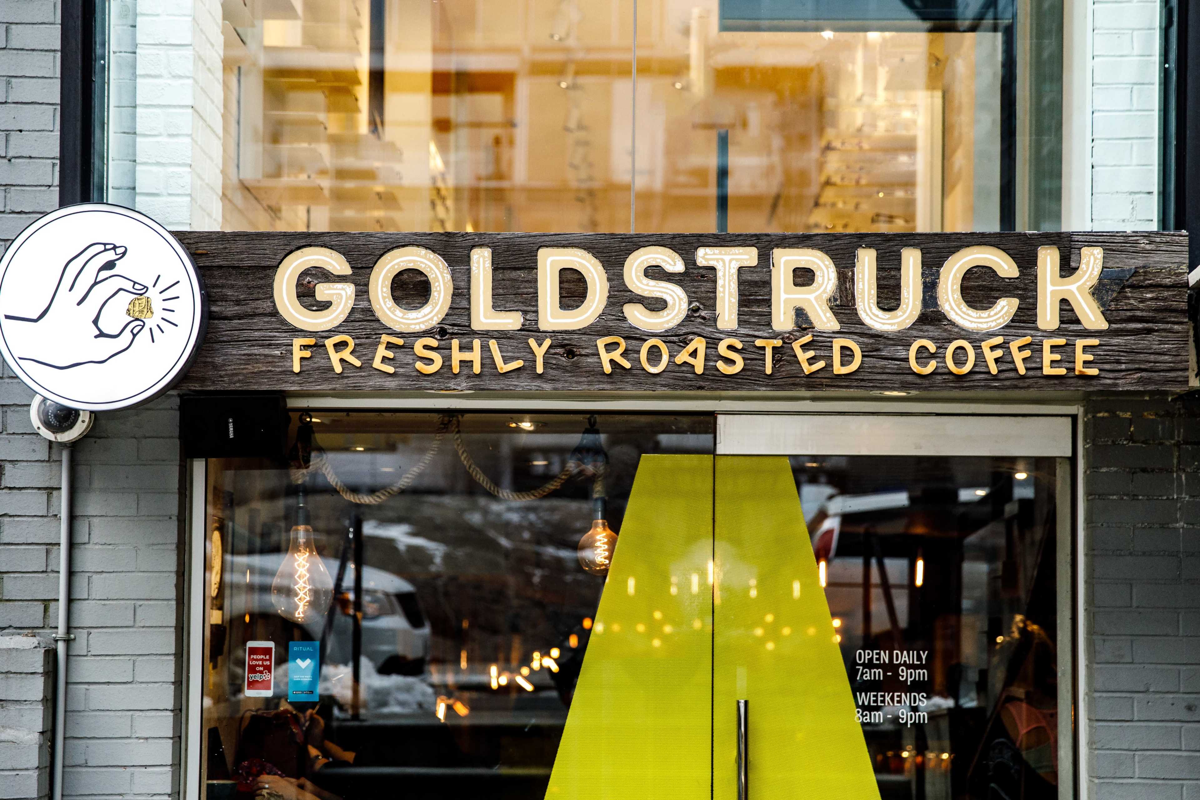 The image features the storefront of a coffee shop named "Goldstruck," with a large wooden sign displaying the shop's name and the tagline "Freshly Roasted Coffee."
