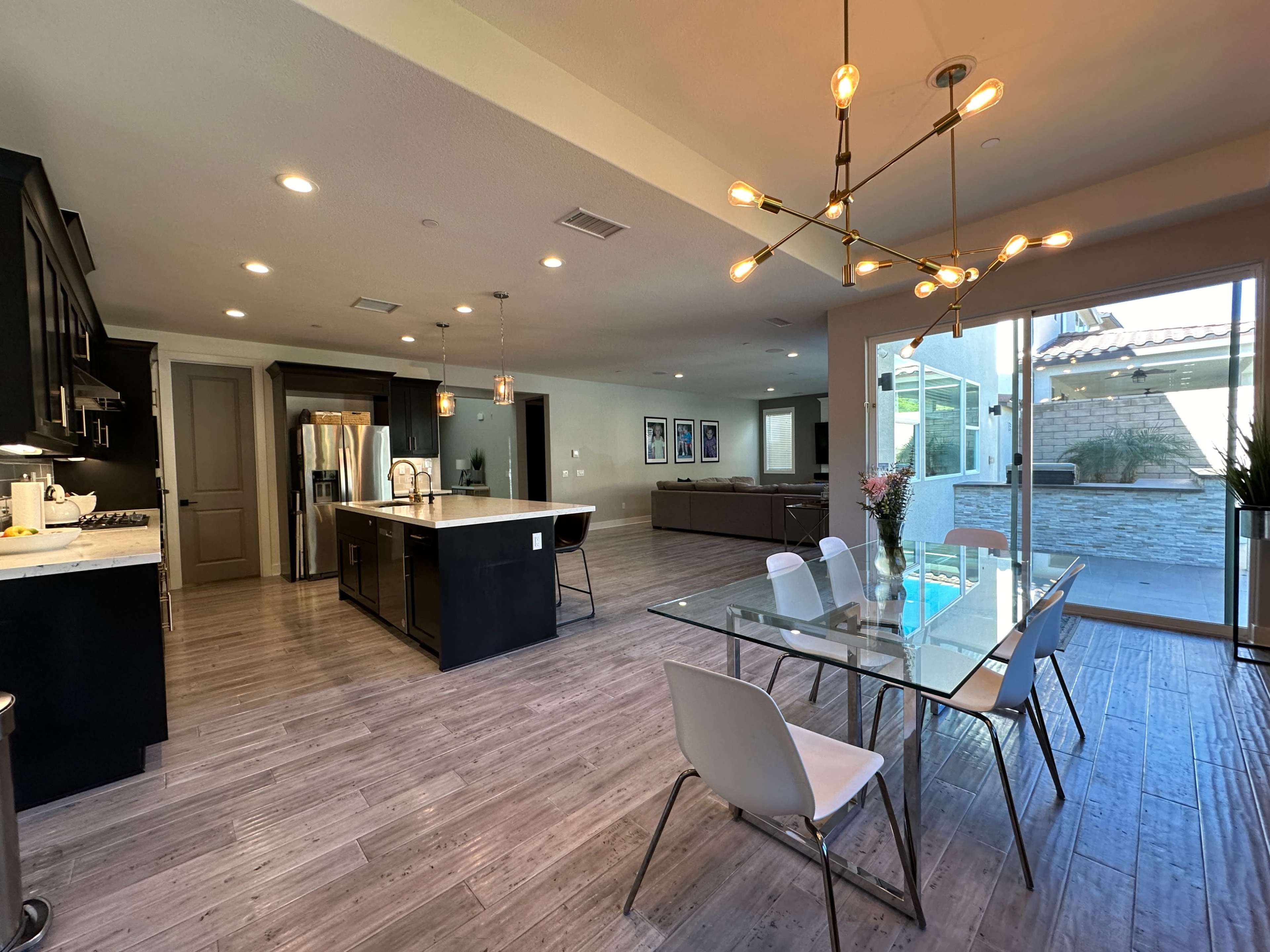 A modern kitchen and dining area featuring an island with a sink, a glass dining table, and large sliding glass doors leading to an outdoor space.