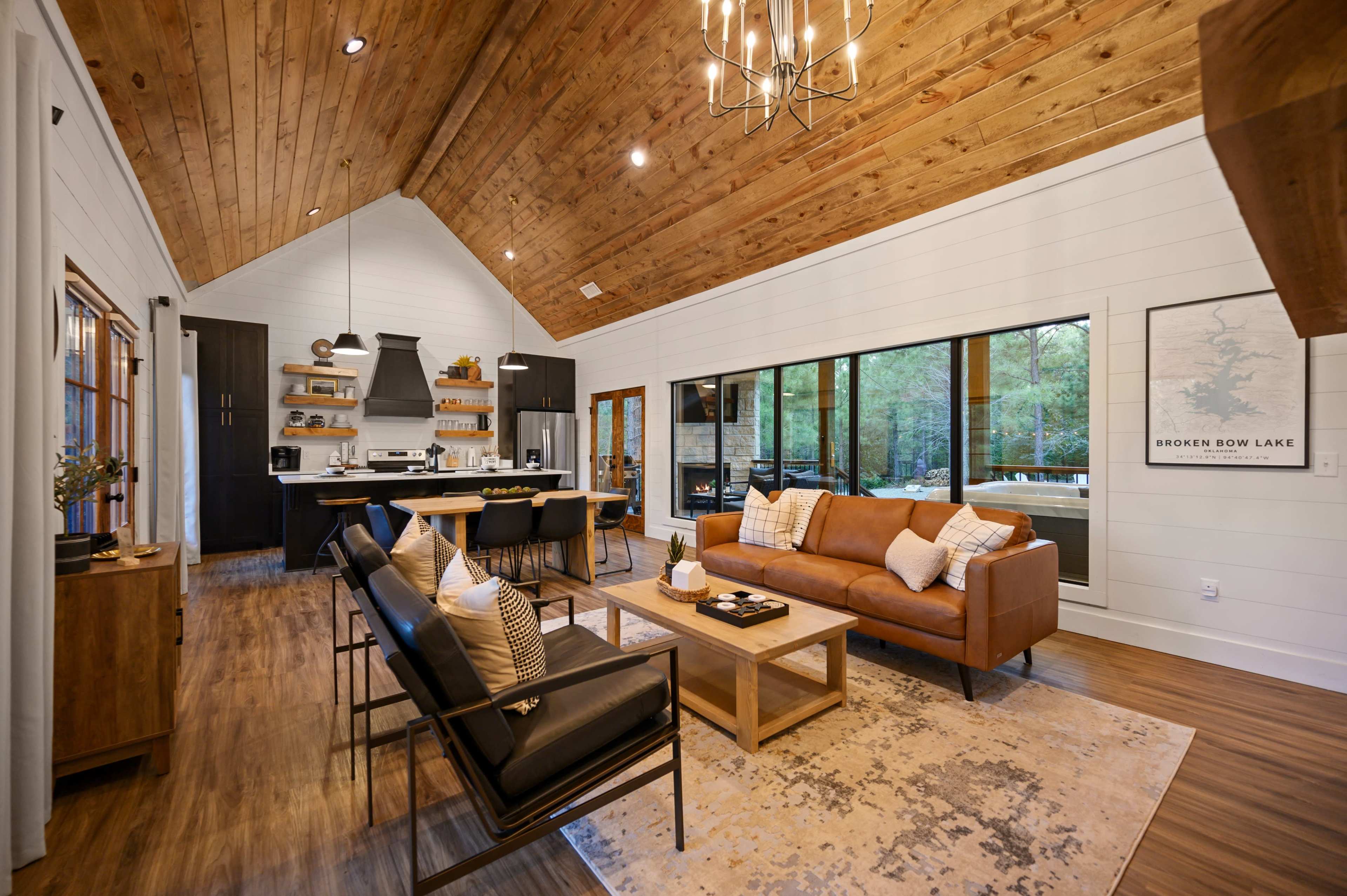 A modern living area with wooden ceilings, a leather sofa, and large windows overlooking a natural setting.