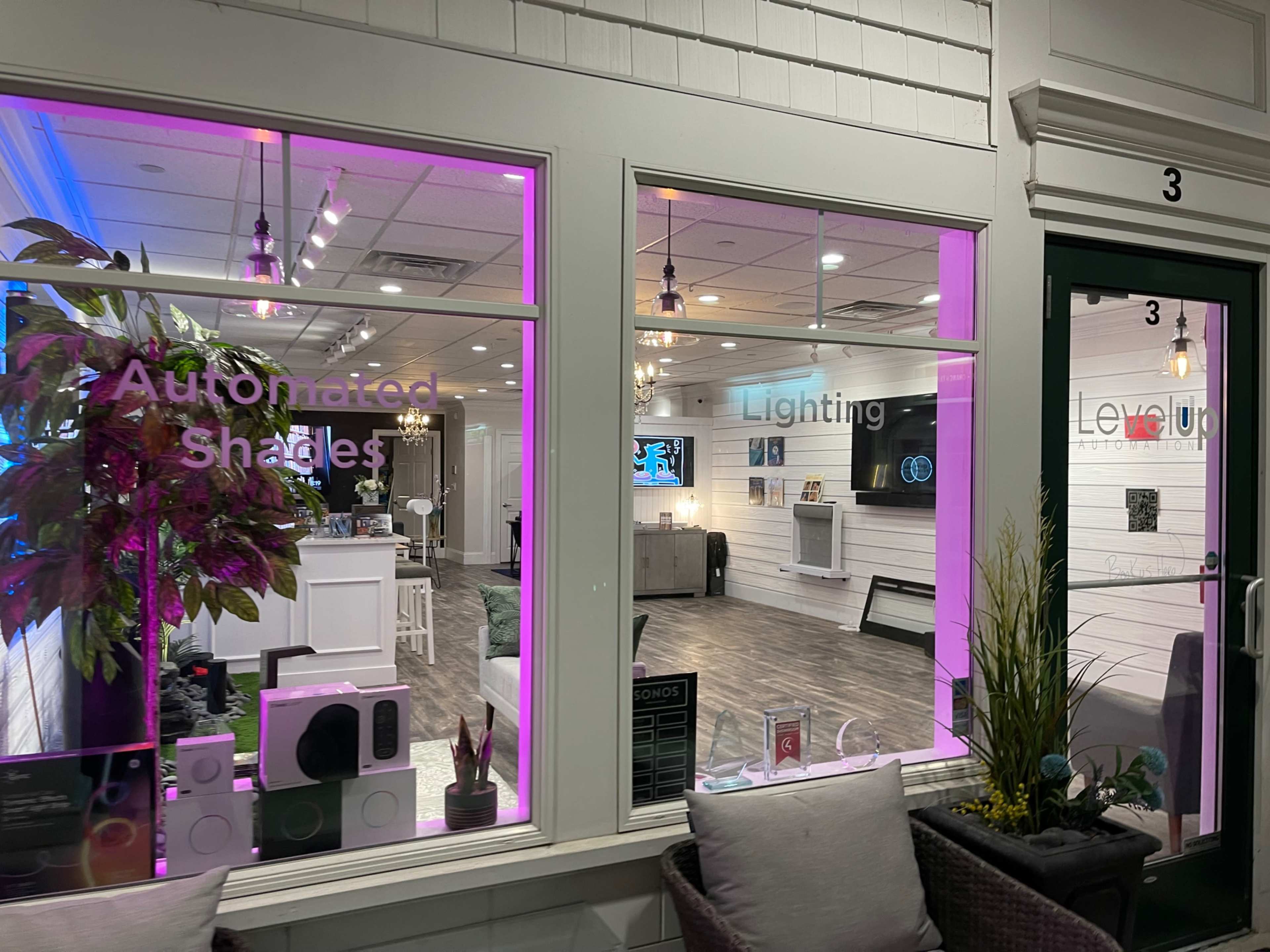 The image shows a storefront with large windows displaying the words "Automated Shades," "Lighting," and "Level Up," along with a modern interior setup visible through the glass.