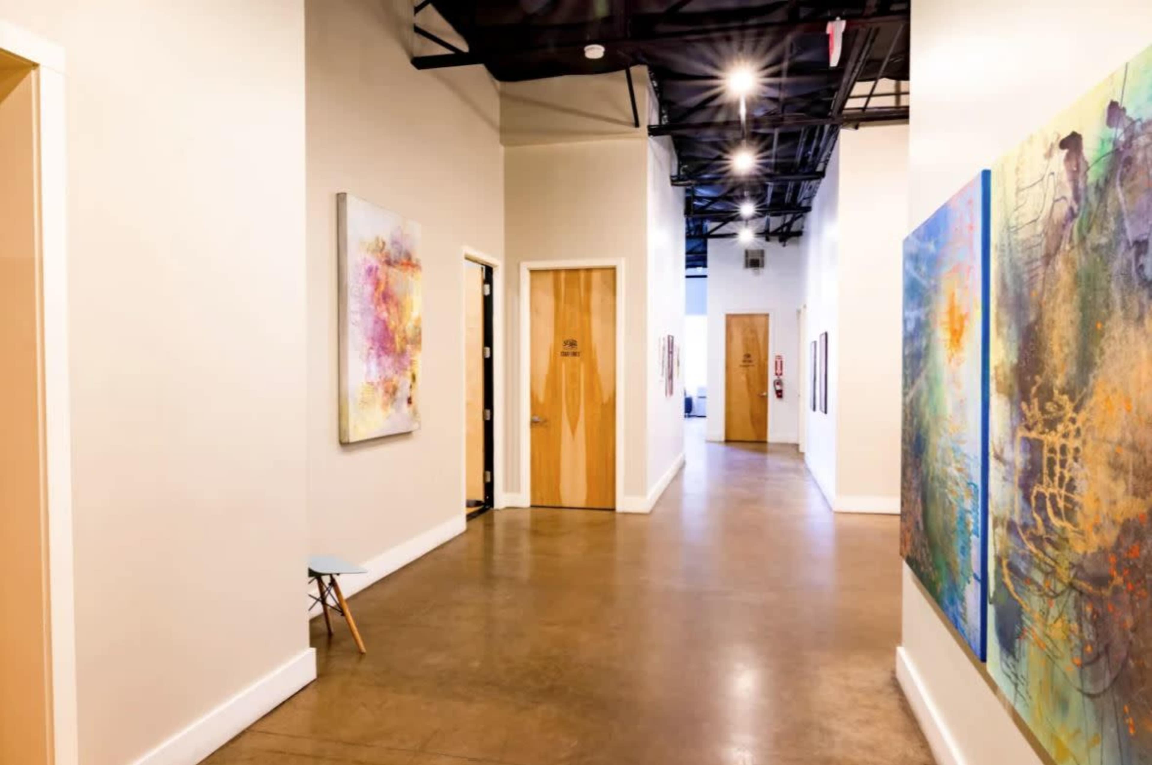 A well-lit hallway with artwork on one wall and wooden doors lining either side.