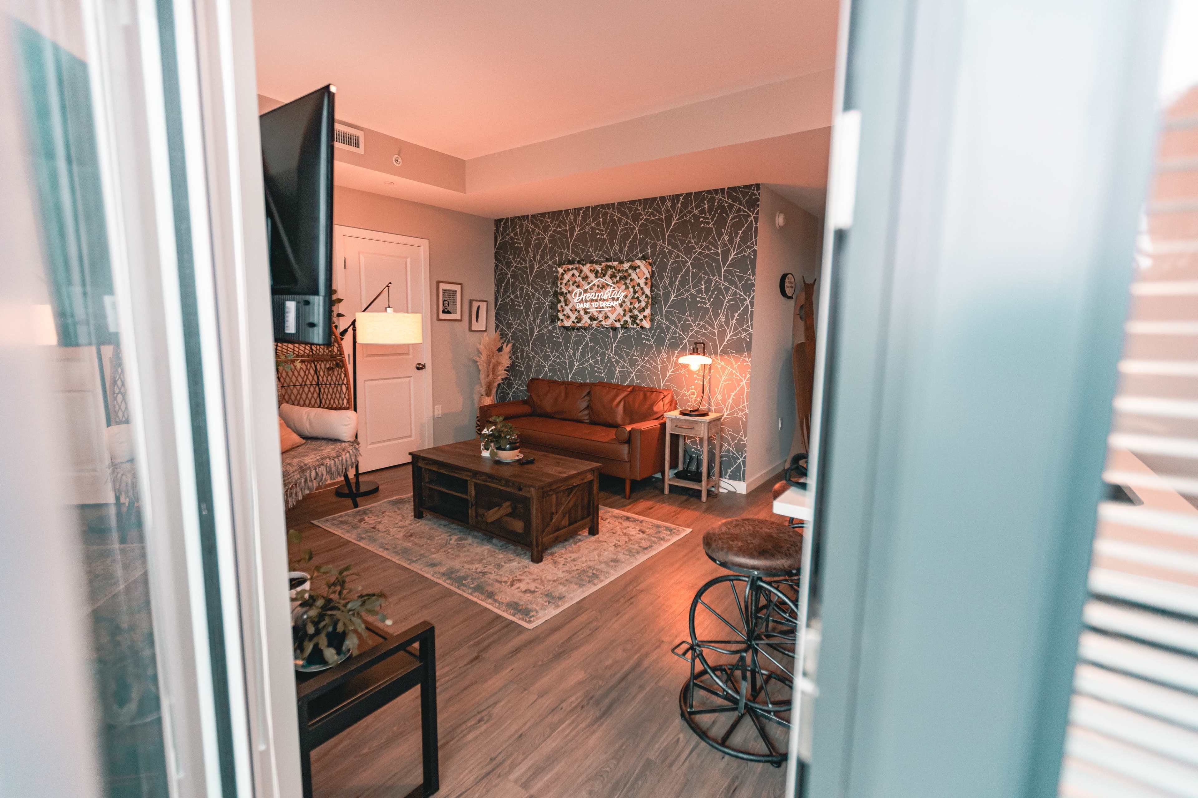 A cozy living room features a brown leather sofa, a wooden coffee table, and a patterned area rug under soft lighting.