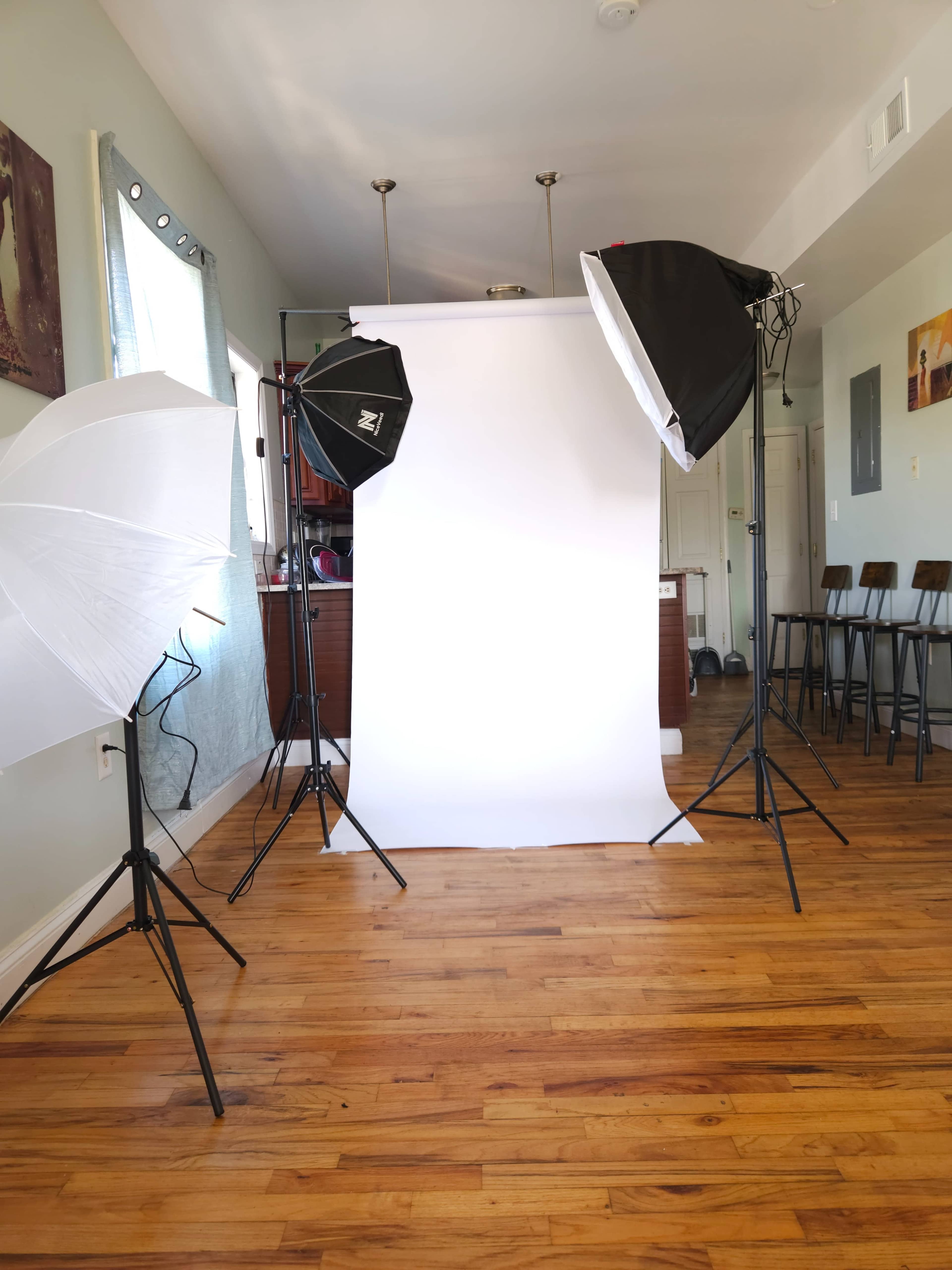 The image shows a photography setup with softbox lights and a white backdrop in a room with wooden flooring.