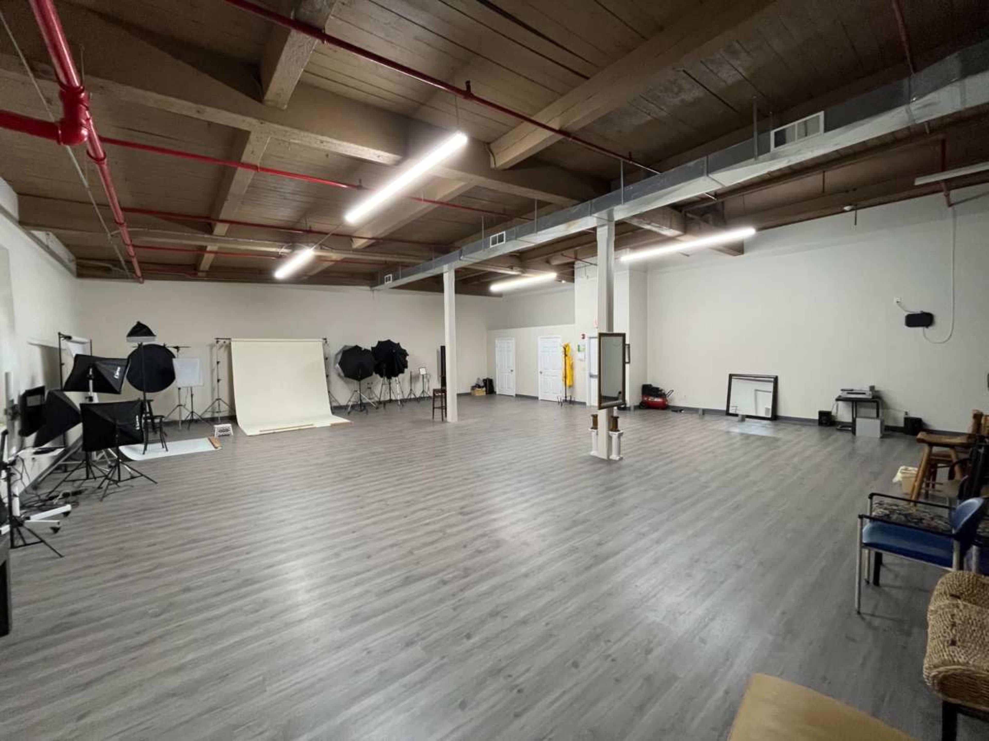 The image shows a spacious photography studio with various lighting equipment and backdrops arranged around the room.