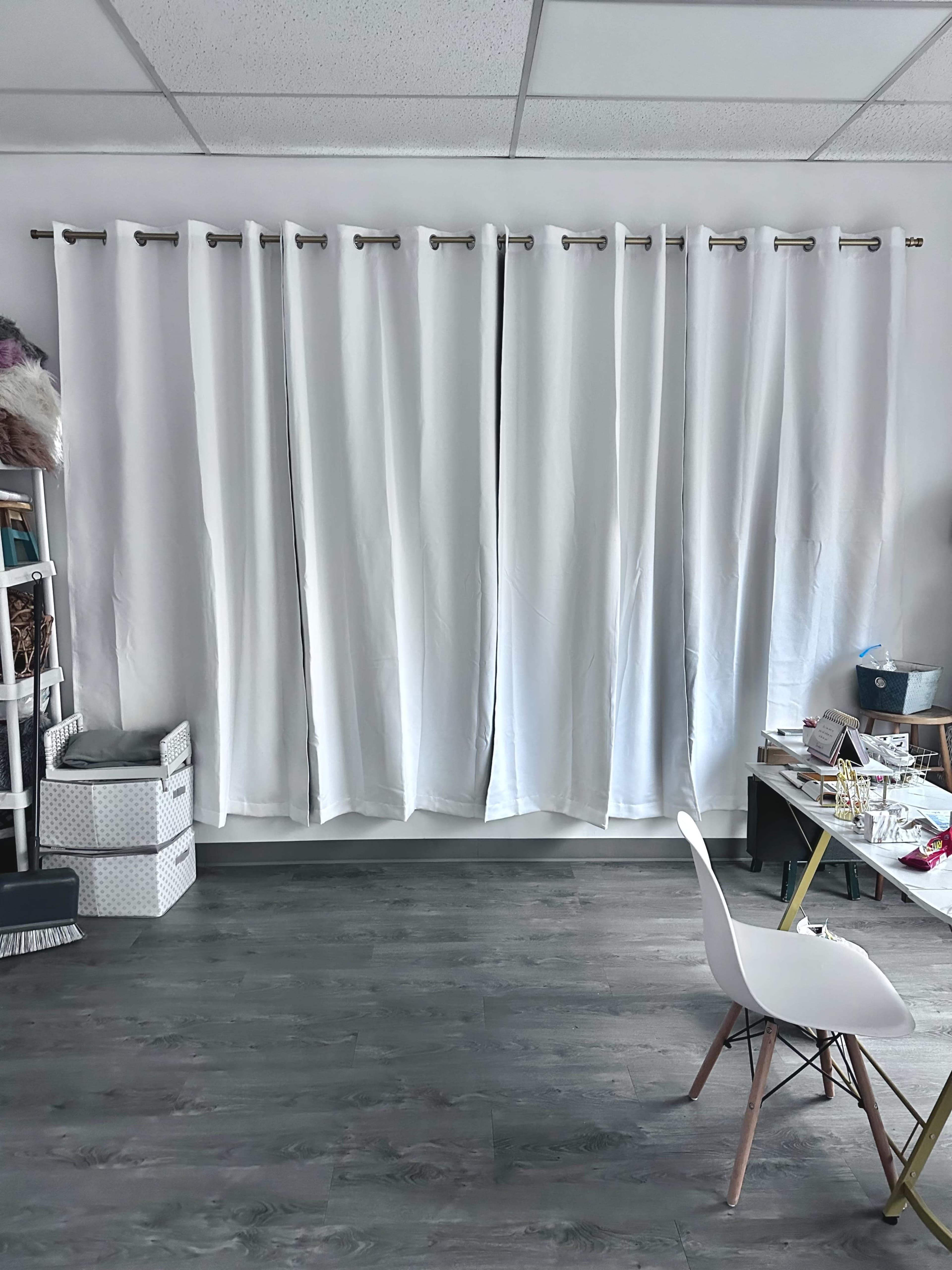 A room with white curtains covering a window, a light-colored chair, and a table with various craft supplies.