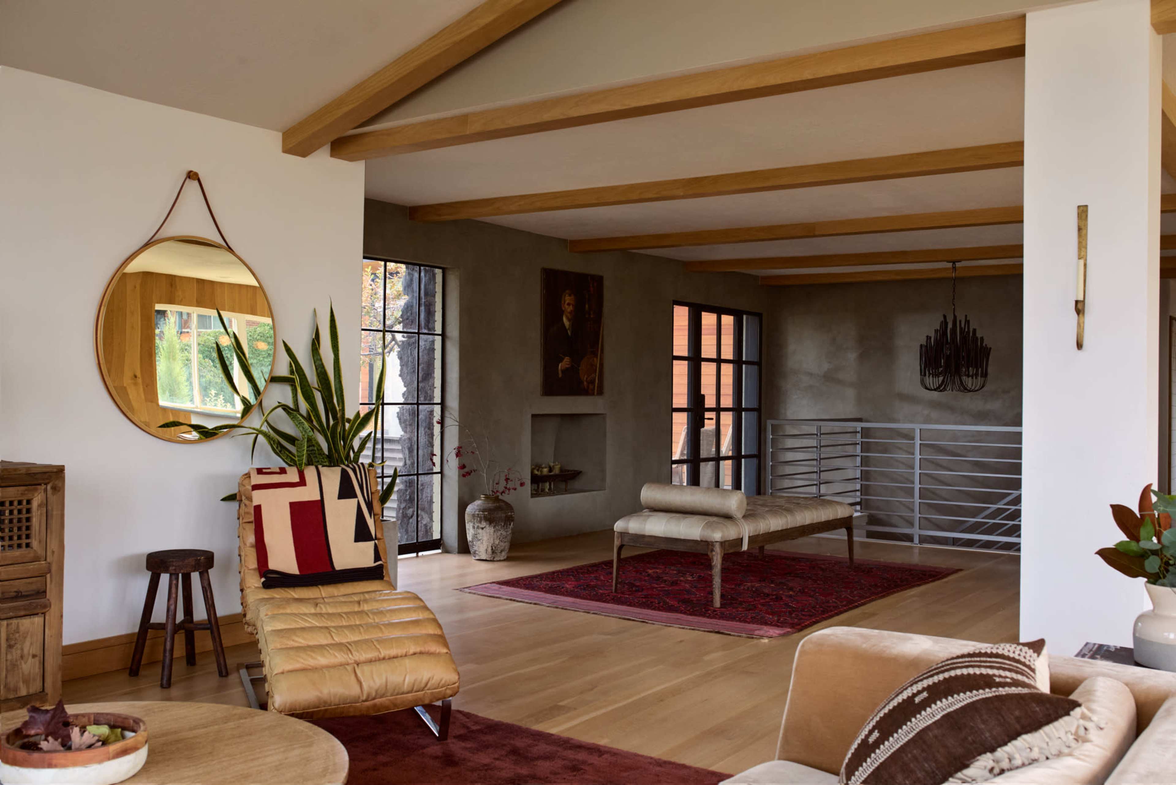 The image shows a modern living space with wooden beams, a circular mirror, a bench, and a mixture of decorative elements on the walls and floor.
