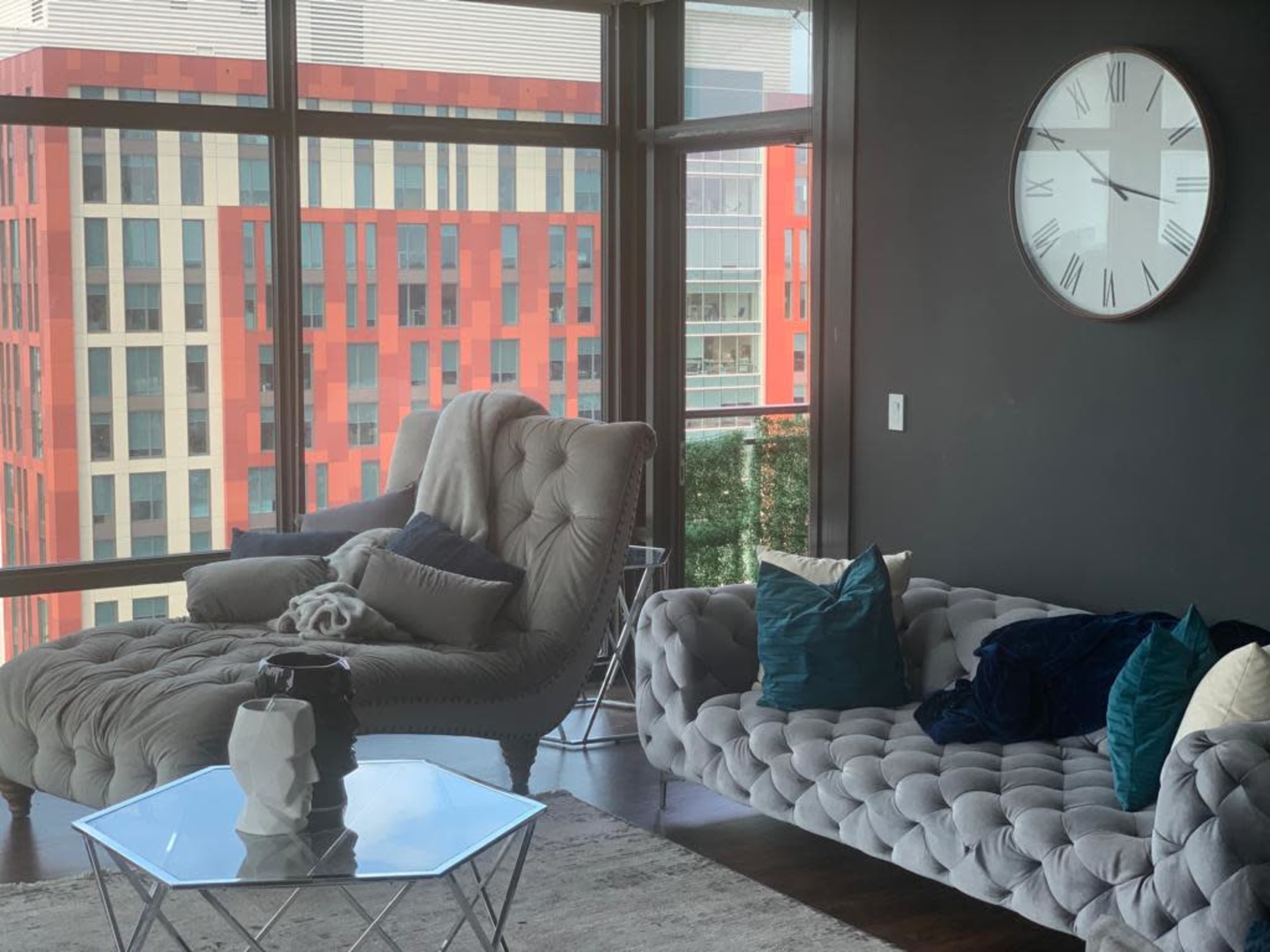 A modern living room with two stylish tufted sofas, a glass coffee table, and large windows showcasing an urban view.