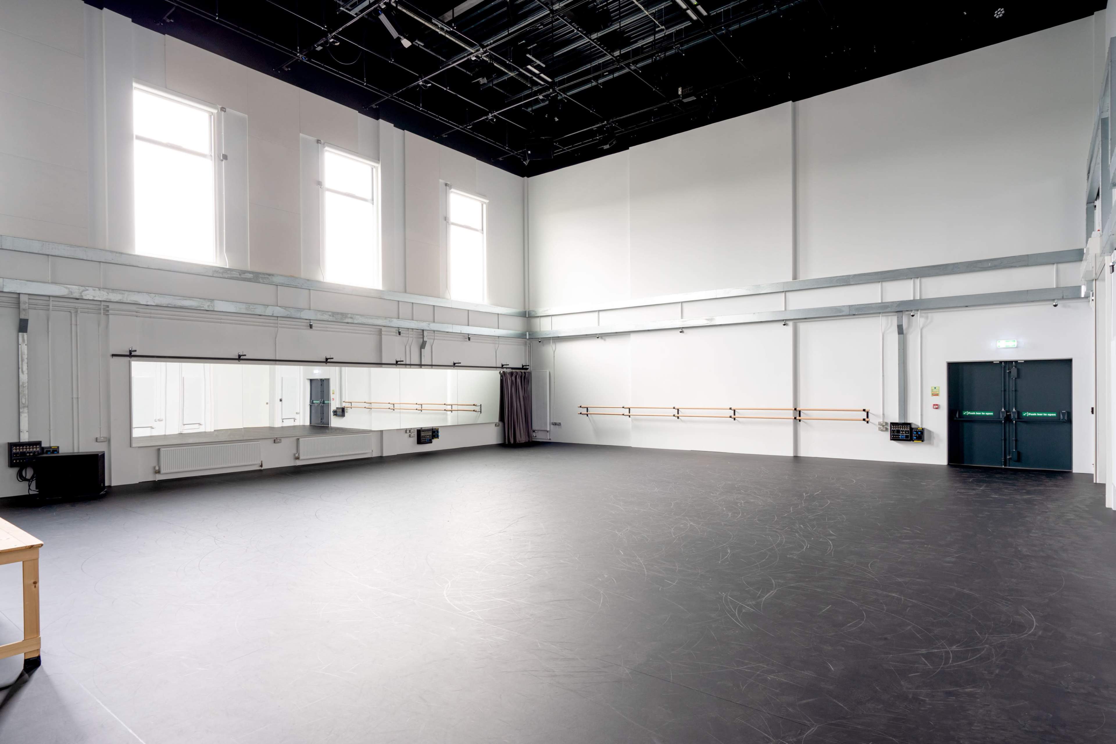A spacious, empty dance studio with large windows, mirrored walls, and a ballet barre along one side.