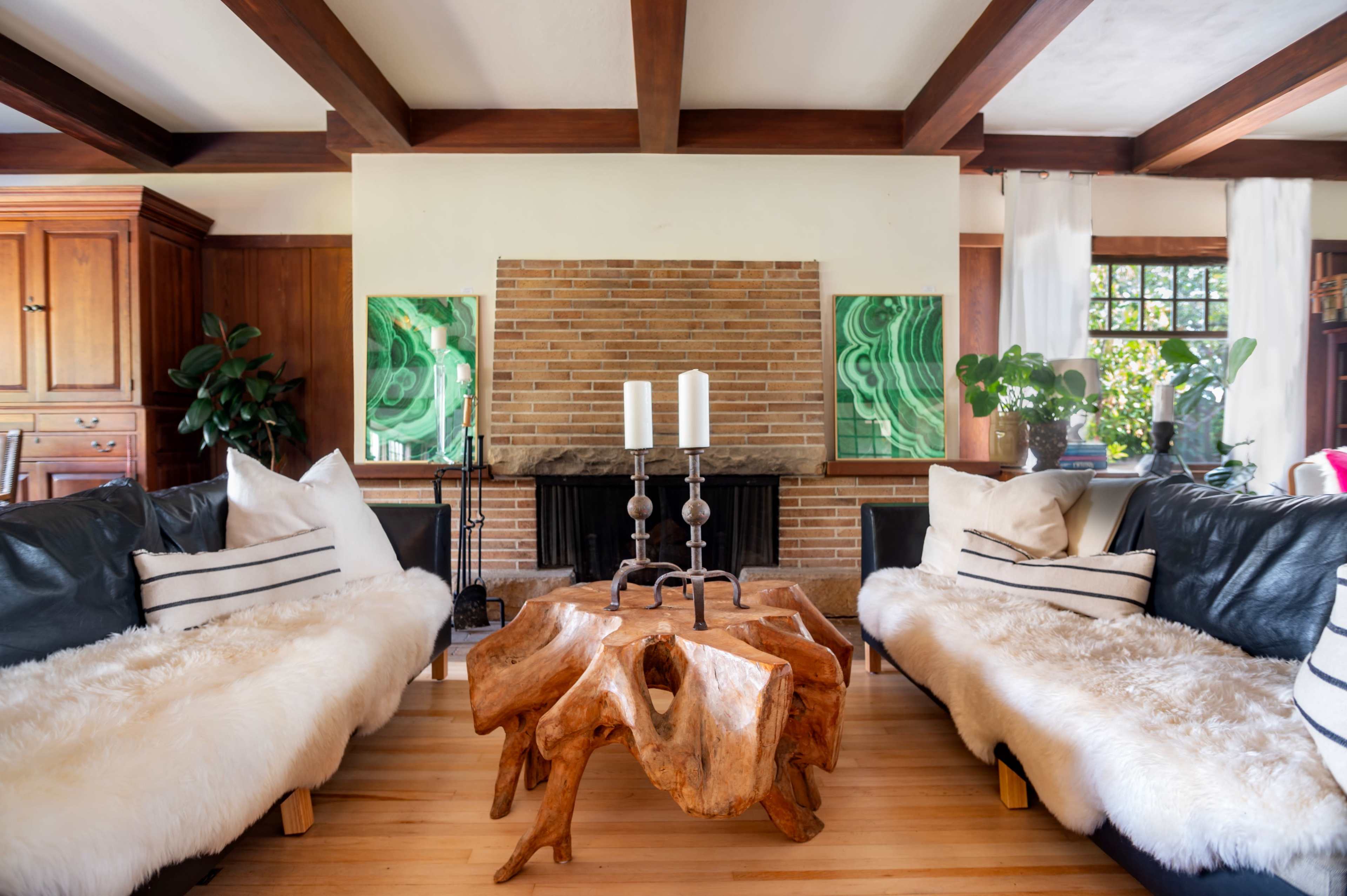 The living room features two leather sofas with fur throws facing a wooden coffee table and a brick fireplace, accented by two green decorations on the wall.