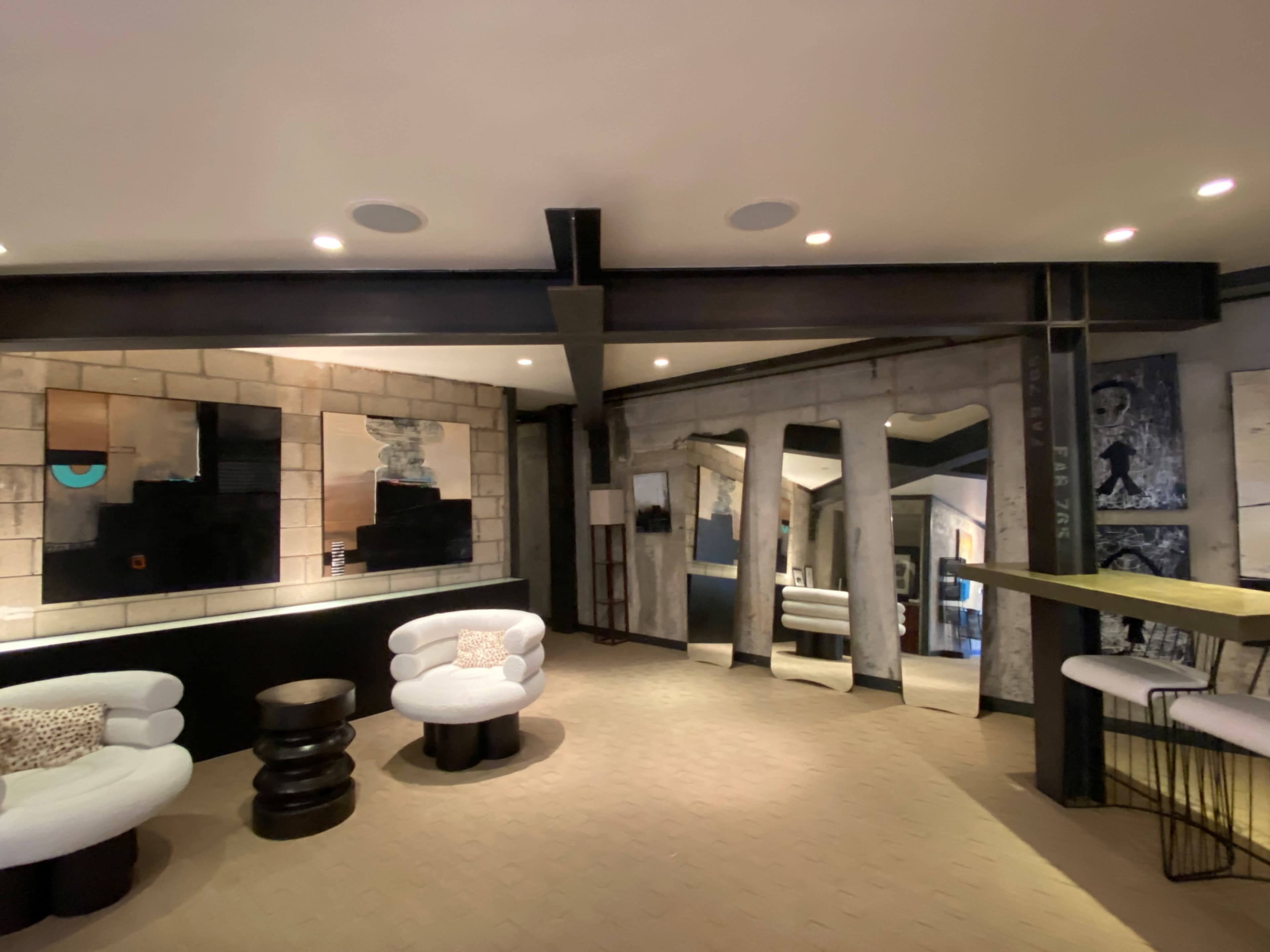 A modern interior space with circular seating arrangements, mixed media artworks on the walls, and a wooden bar counter with a minimalist design.
