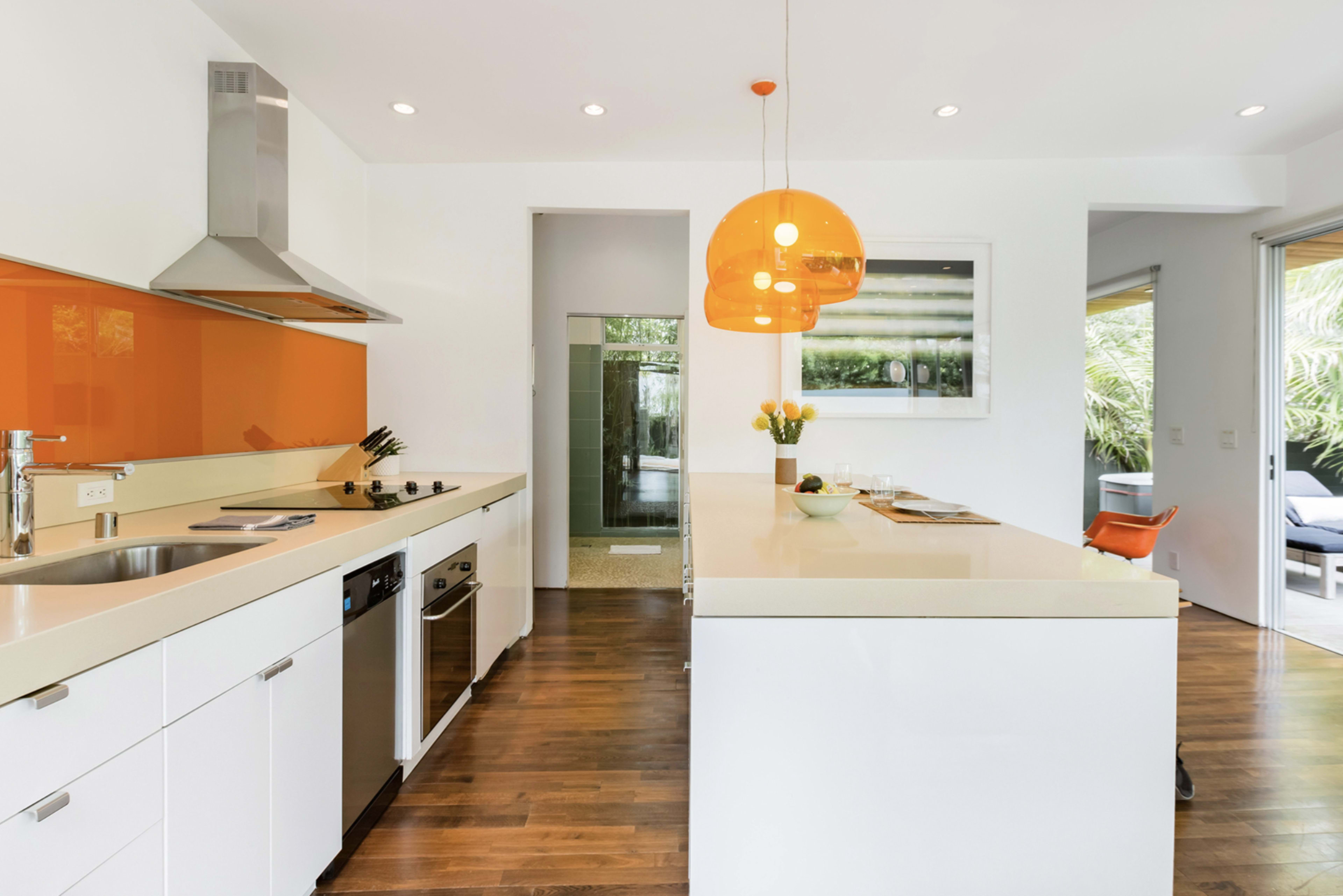 The image shows a modern kitchen featuring white cabinetry, an orange backsplash, and a large island with a pendant light.
