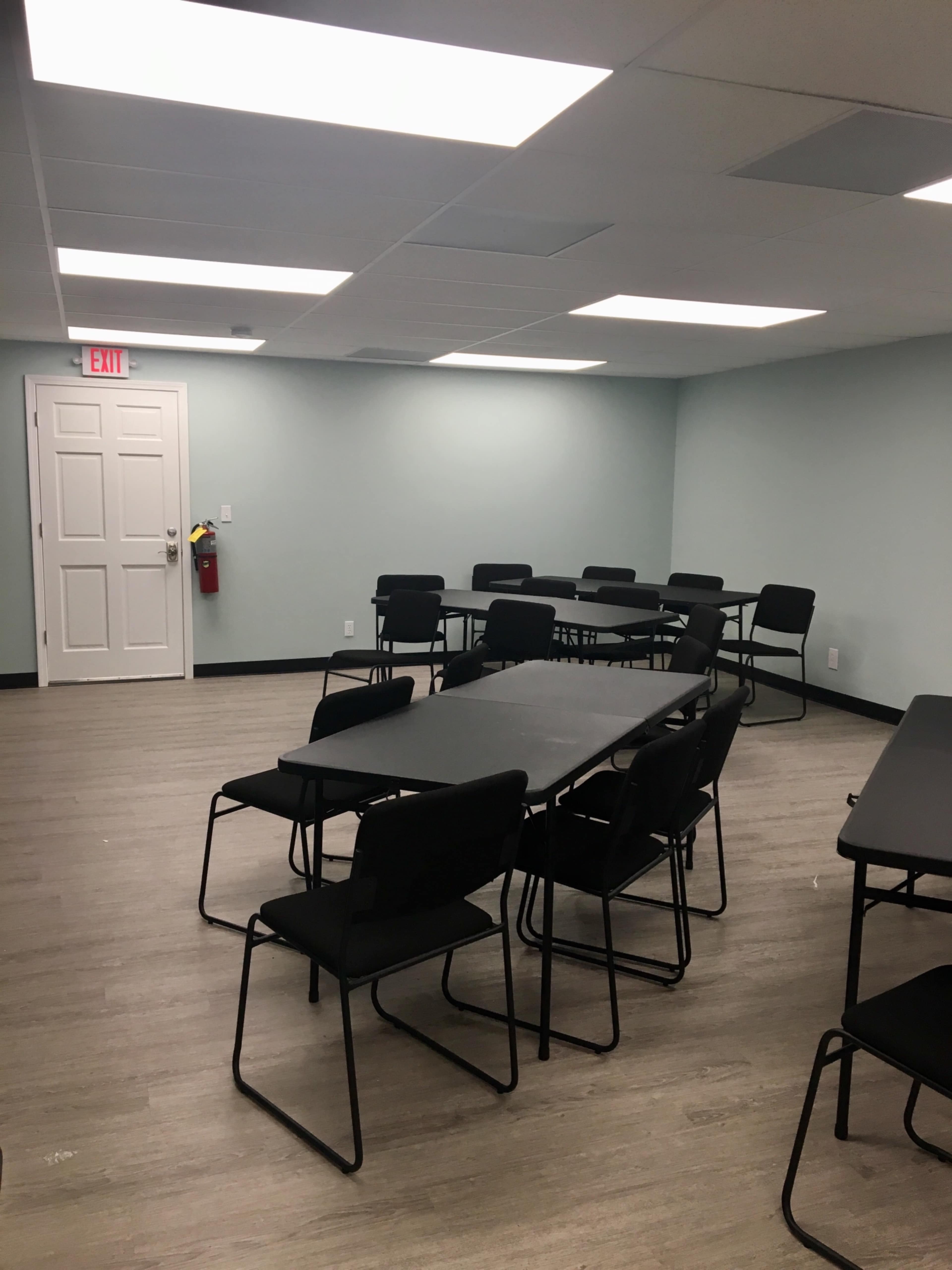 A meeting room with several black folding tables and chairs arranged in a sparse layout against light blue walls.