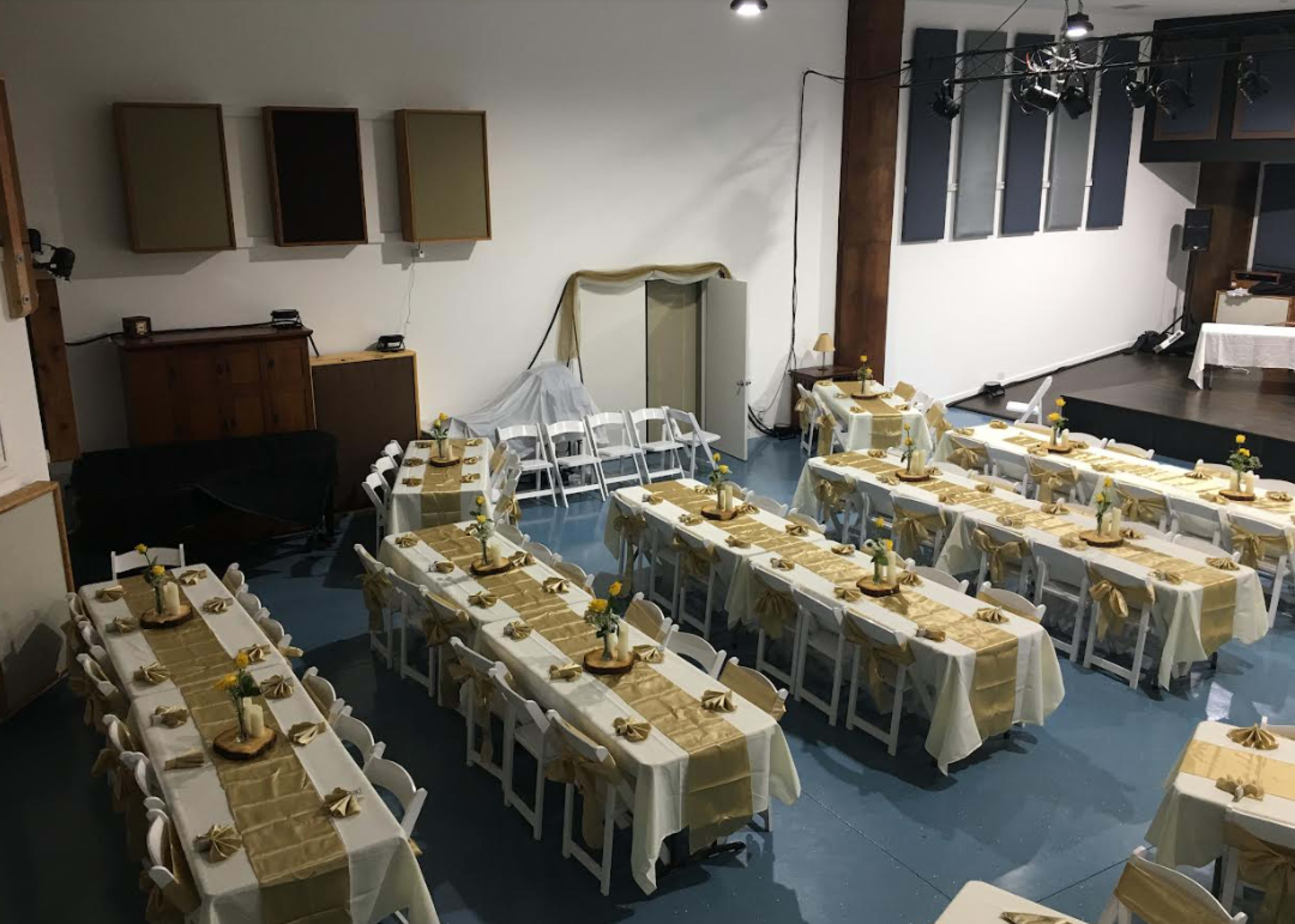 A spacious venue set up with several tables arranged in rows, each covered in cream-colored tablecloths and adorned with yellow floral centerpieces.