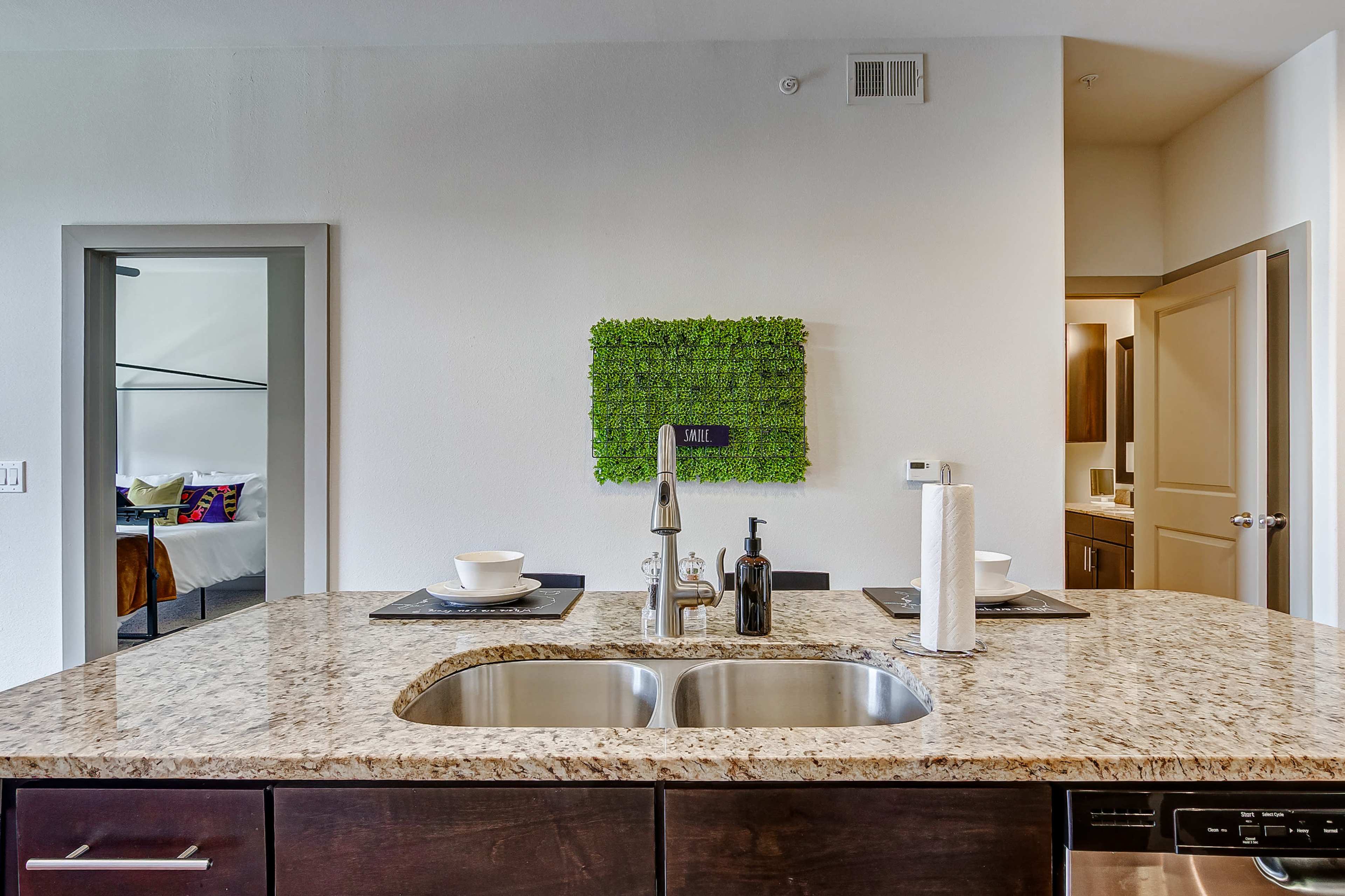 A modern kitchen features a granite countertop with a double sink, decorative wall art, and dining settings arranged on the surface.