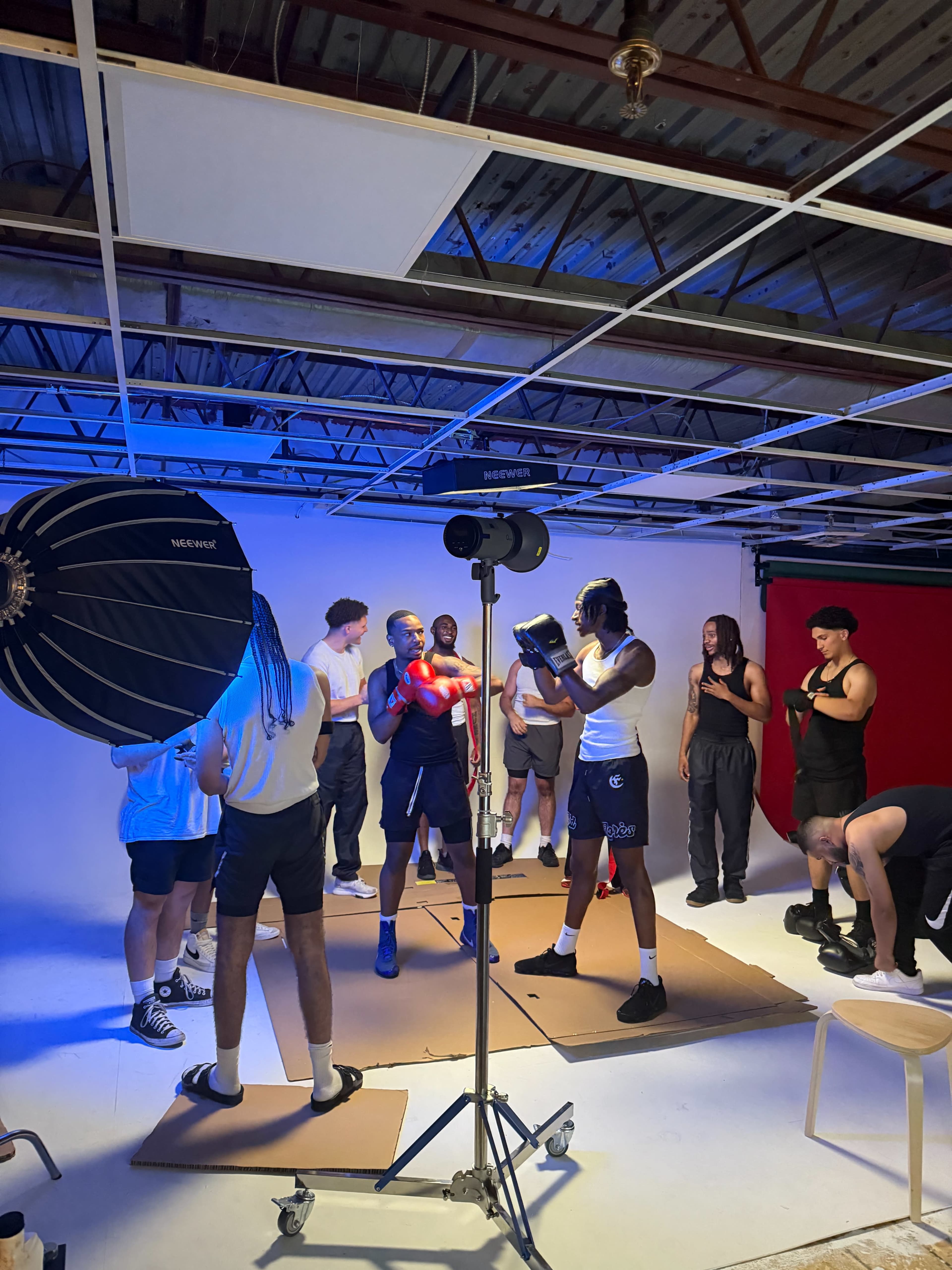 A group of individuals is gathered in a studio, preparing for a boxing photoshoot, with some holding equipment and others adjusting their positions.