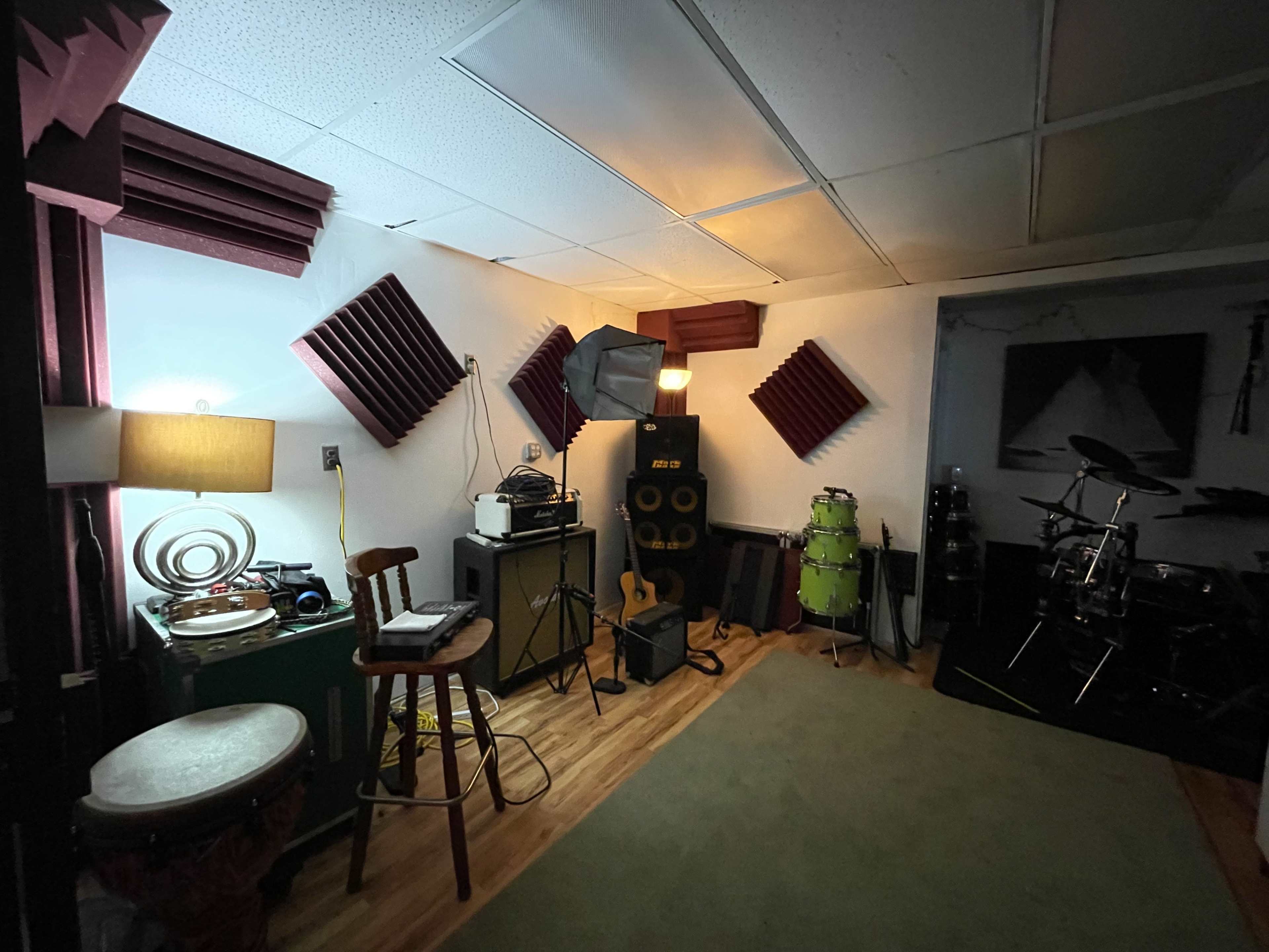 A music rehearsal space featuring various instruments, sound equipment, and acoustic panels on the walls.