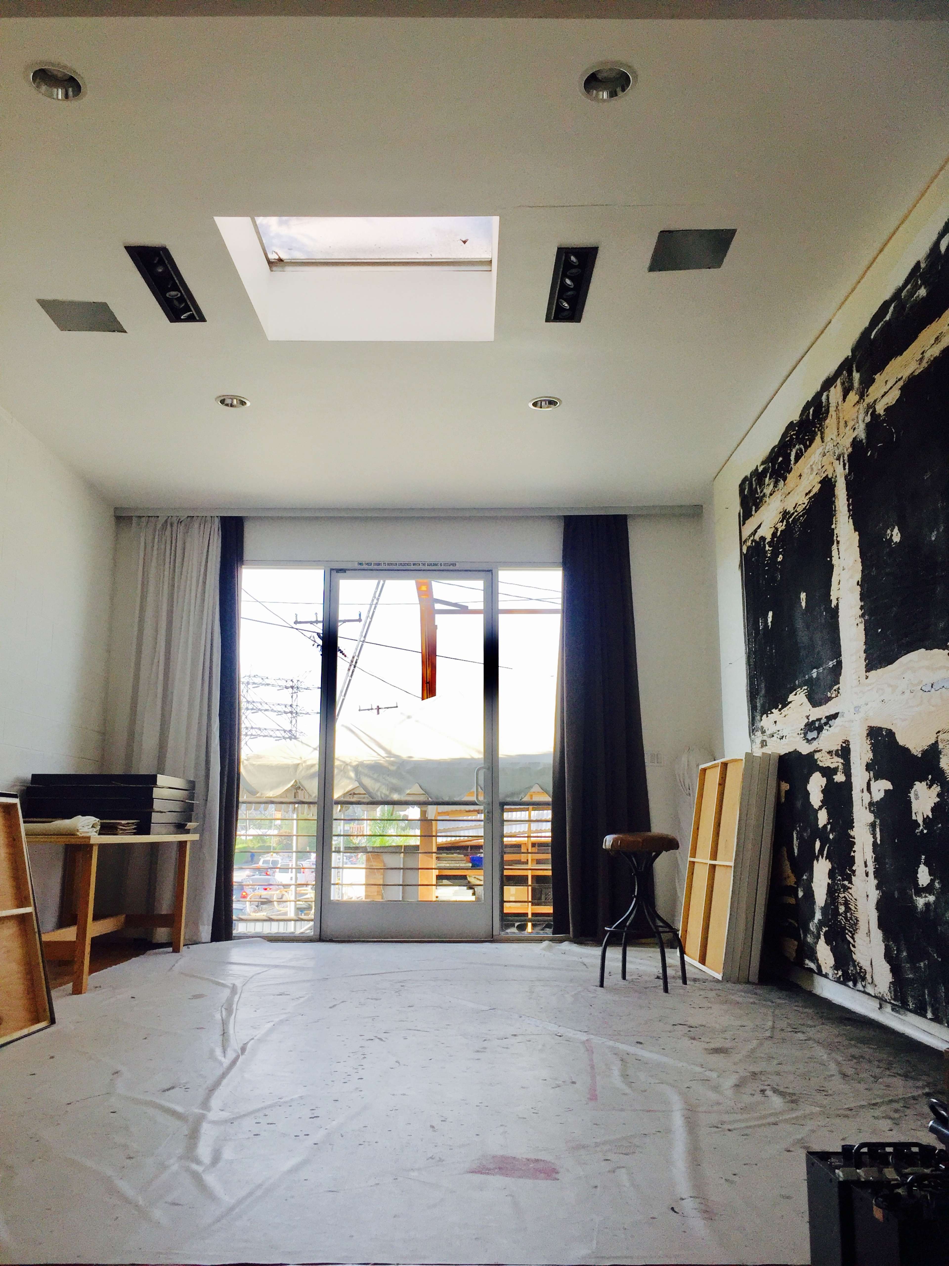 The image shows a sparse room with a large window, a skylight, and various materials stacked against the walls.