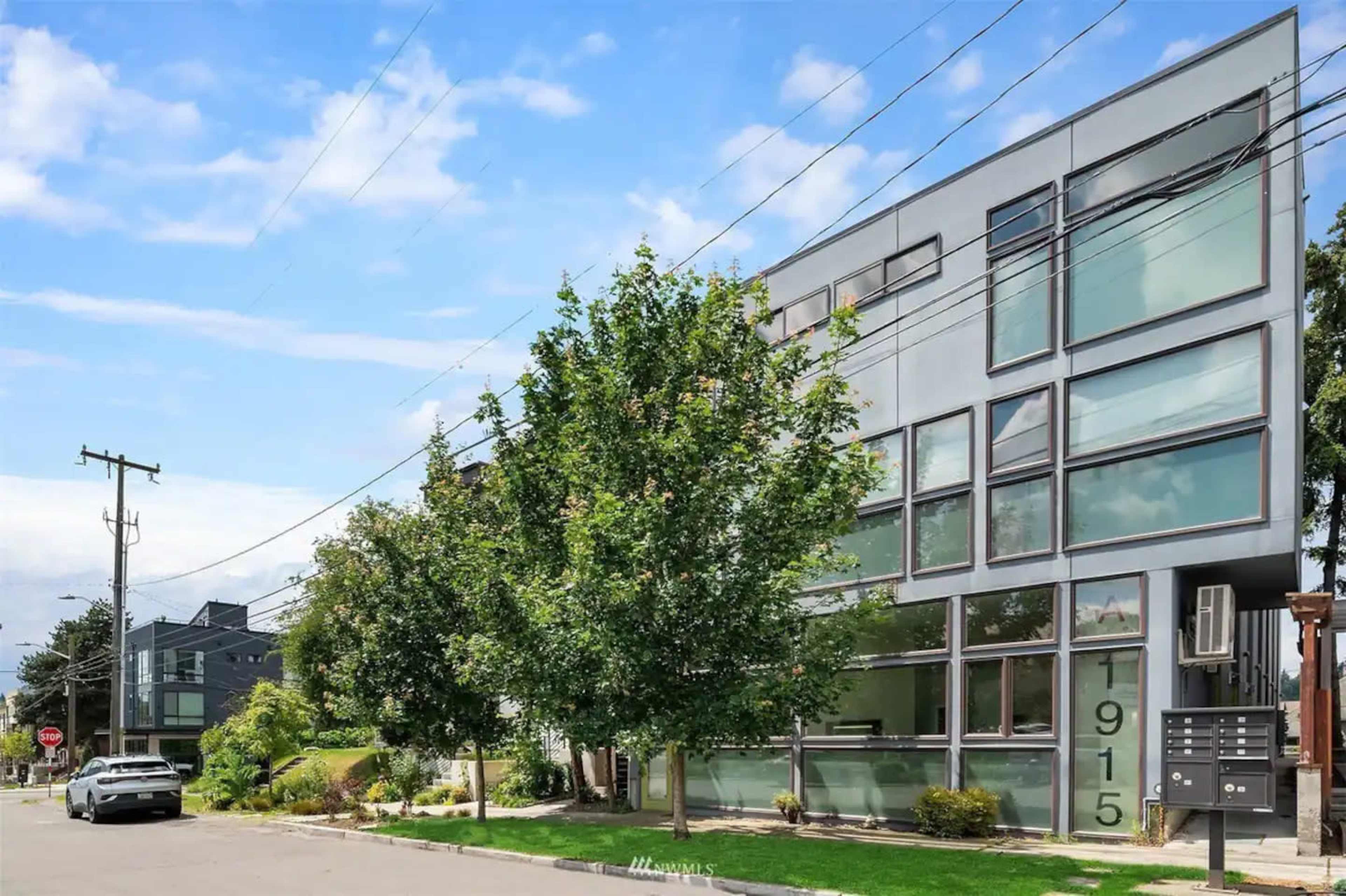 A modern building with large glass windows and a prominent address number 1915 is situated on a tree-lined street.