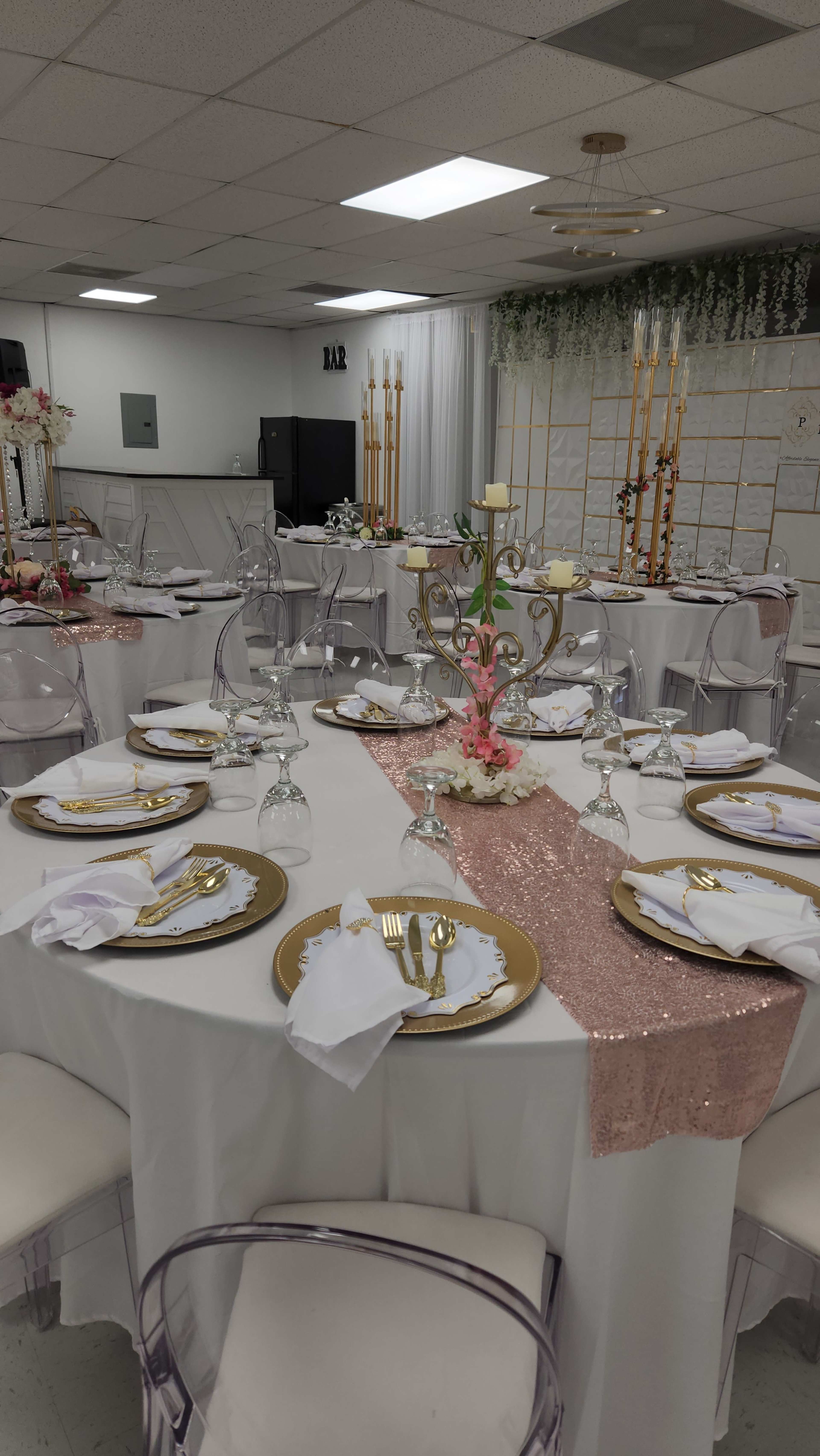 A banquet hall set up for an event, featuring elegantly arranged tables with white tablecloths, gold-rimmed plates, and tall candleholders in a decorated space.