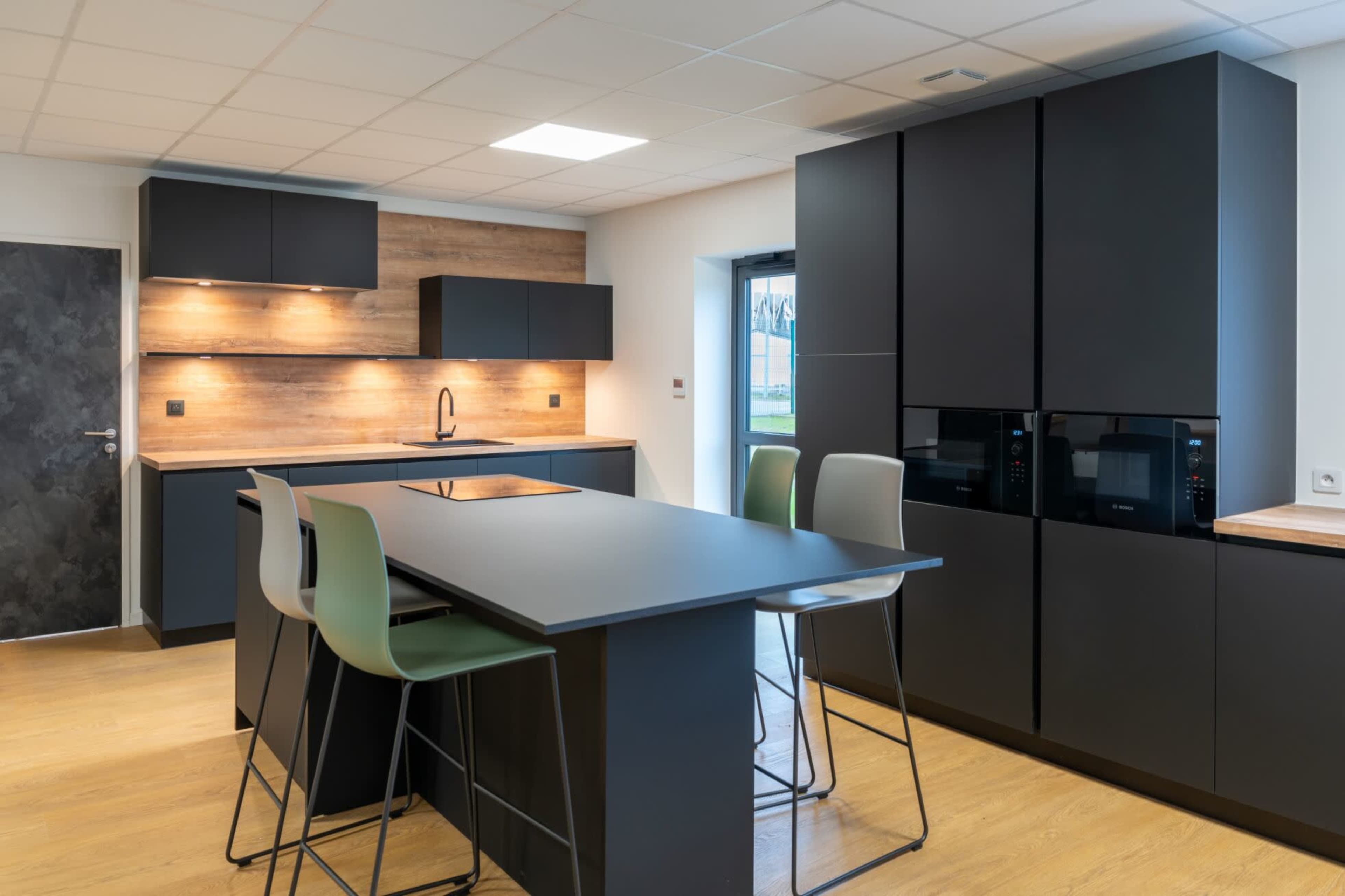 A modern kitchen featuring a dark cabinetry design, a wooden countertop, and a central island with green stools.