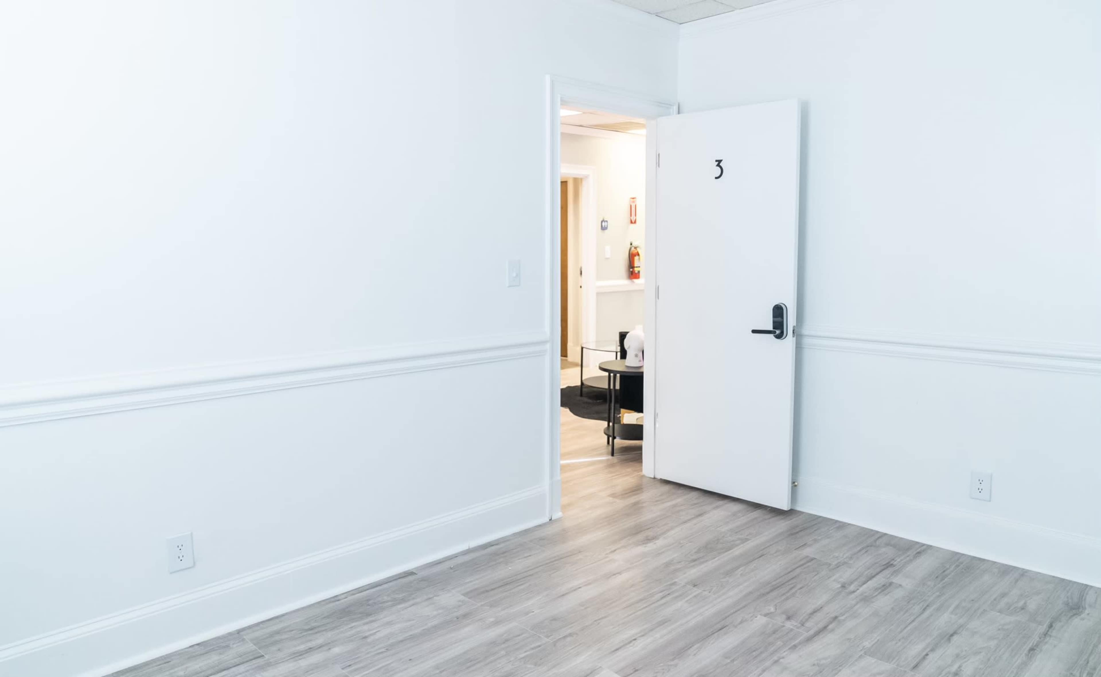 An empty room with white walls, a wooden floor, and an open door labeled "3" leading to another room.