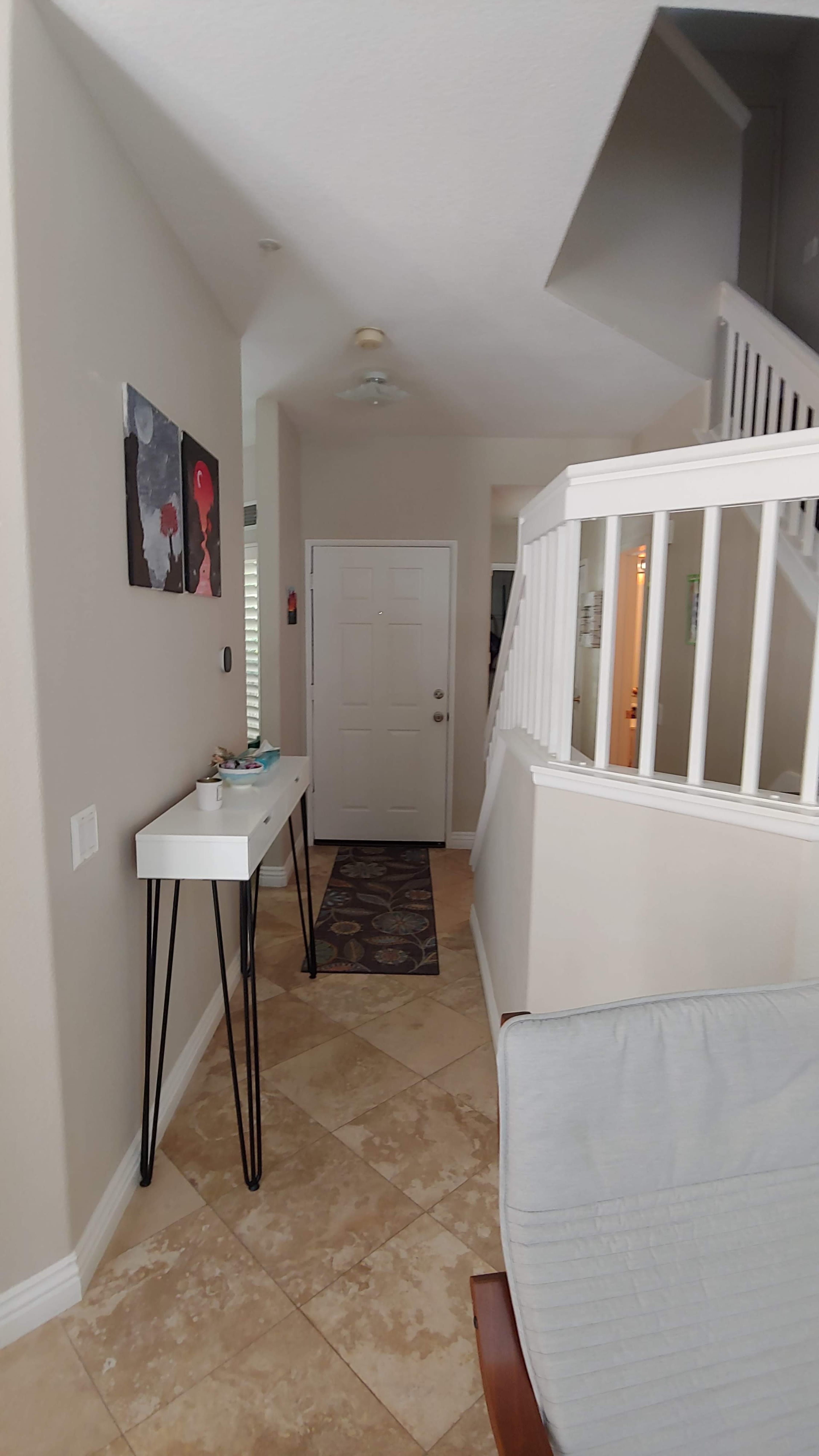 A hallway leading to a front door, with a console table on the left and a staircase on the right.