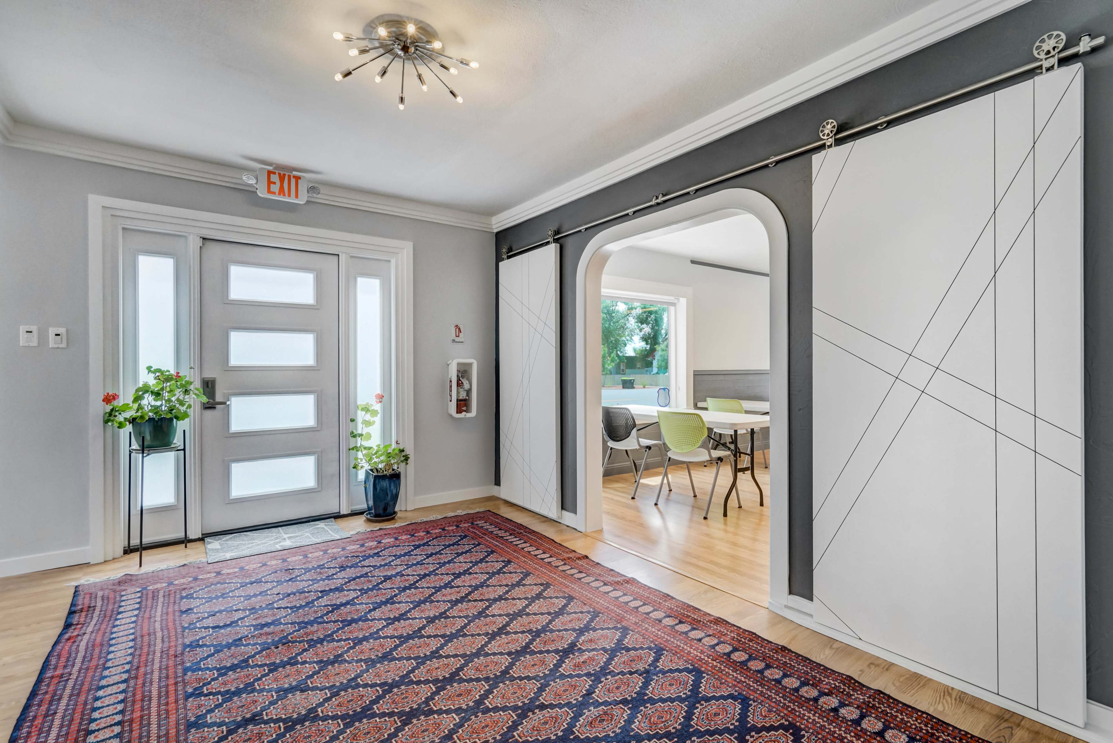A modern entryway with a sleek front door, an archway leading to a dining area, and a patterned rug on the wooden floor.