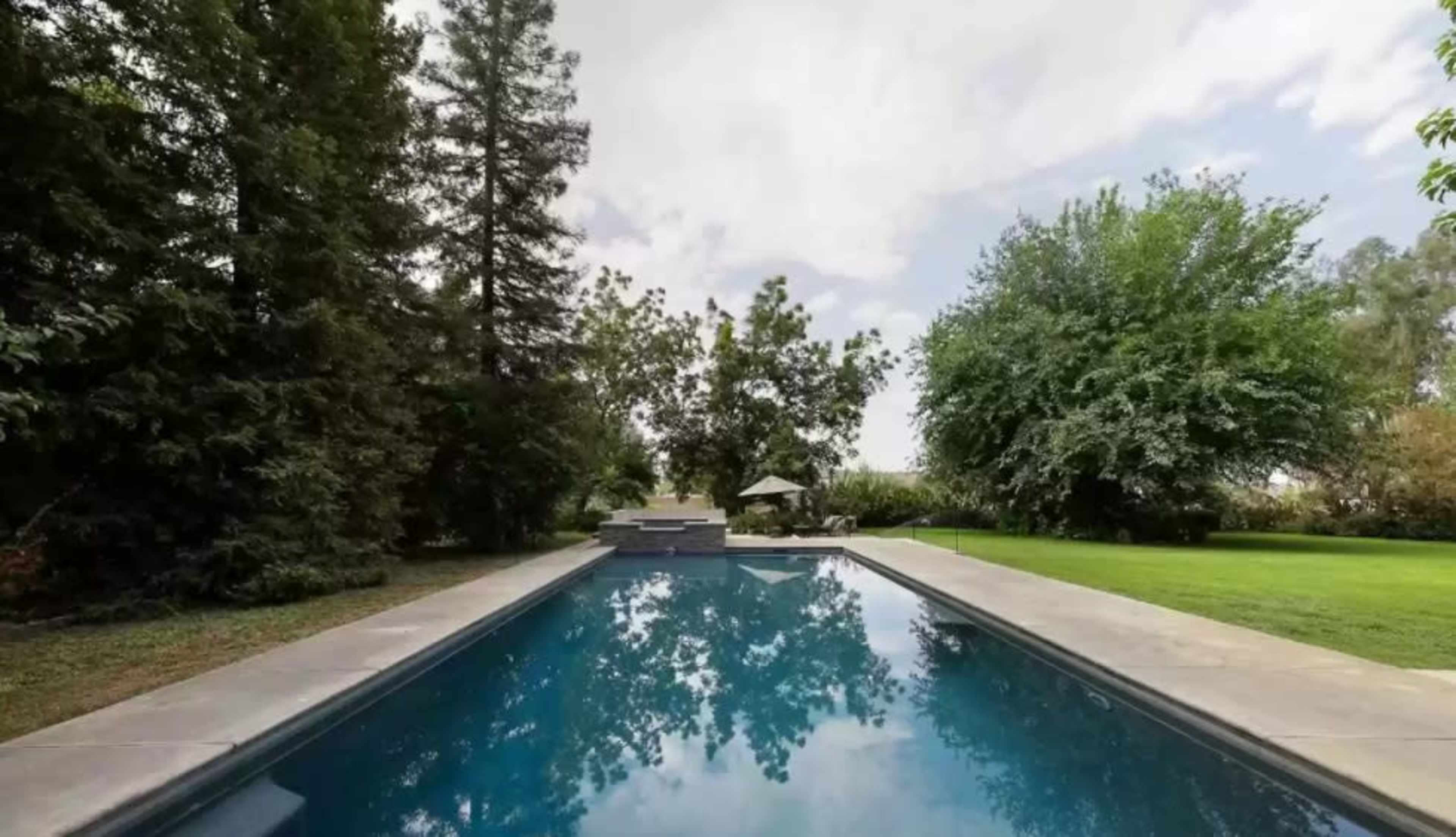 A swimming pool surrounded by greenery and trees under a cloudy sky.