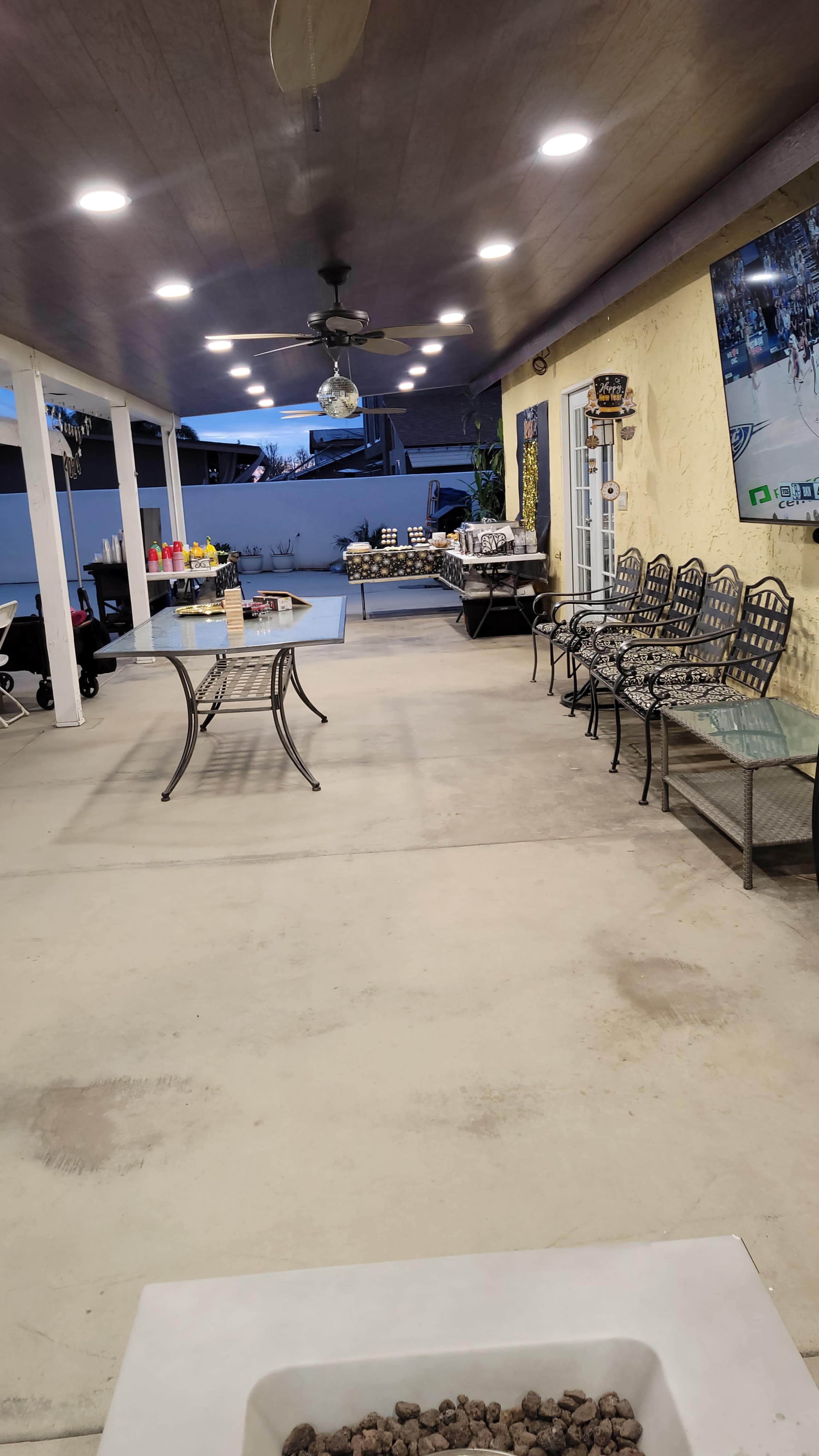 A spacious outdoor patio area furnished with tables and chairs, featuring a fire pit at one end and elements of decor on the walls.