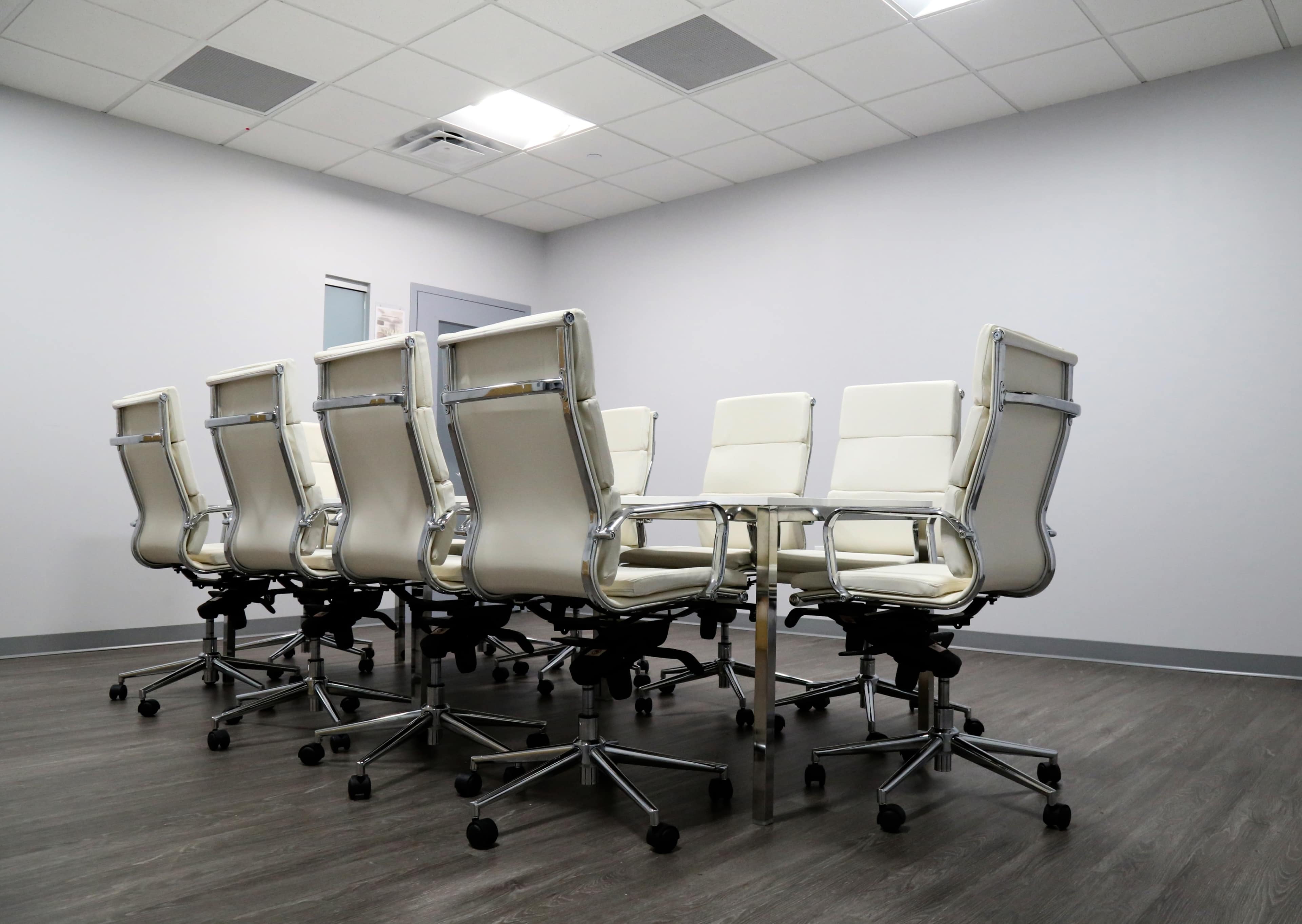 A conference room with a large oval table surrounded by several white office chairs.