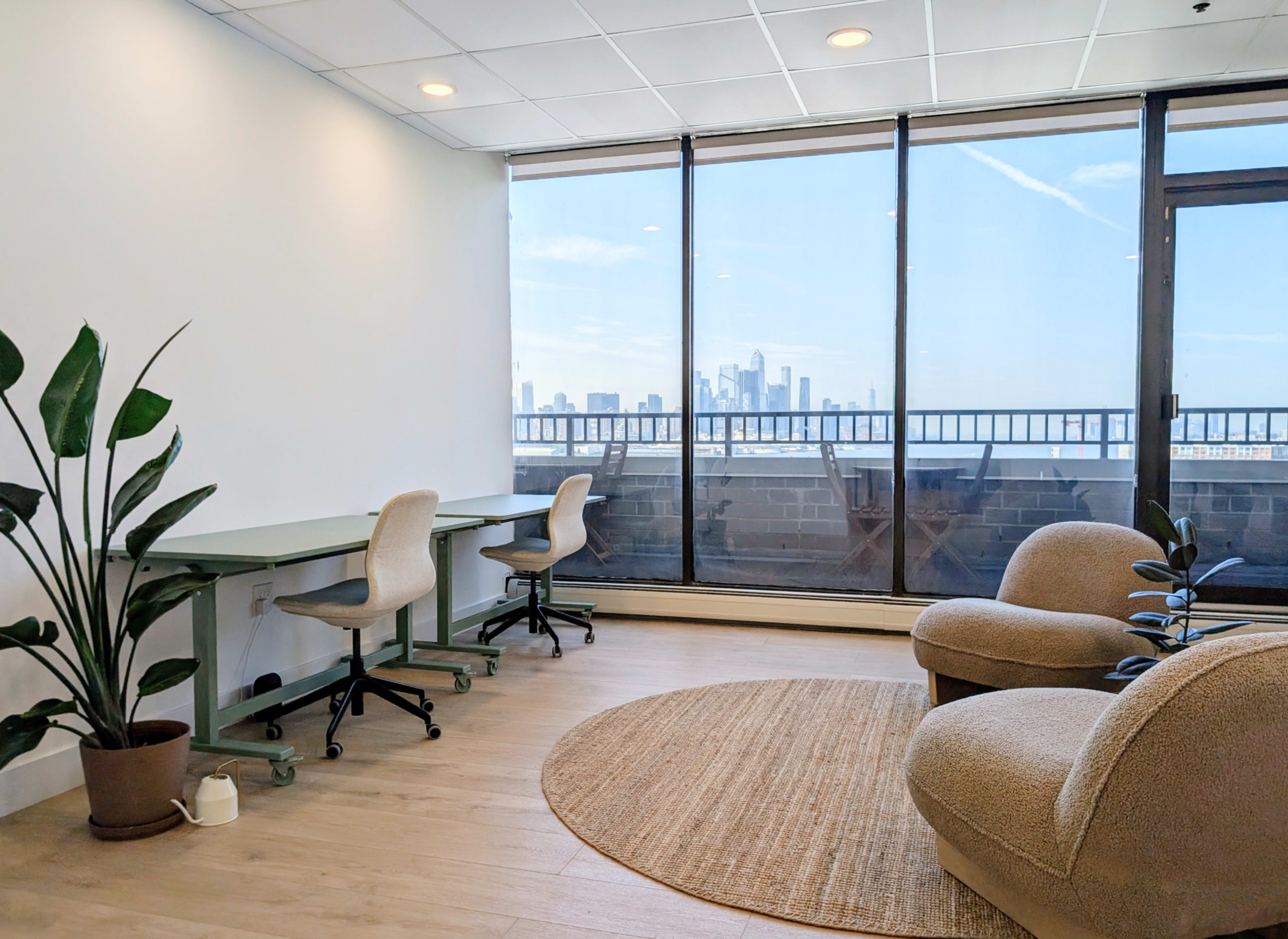 The image shows a modern office space with two desks facing large windows that offer a view of a city skyline.