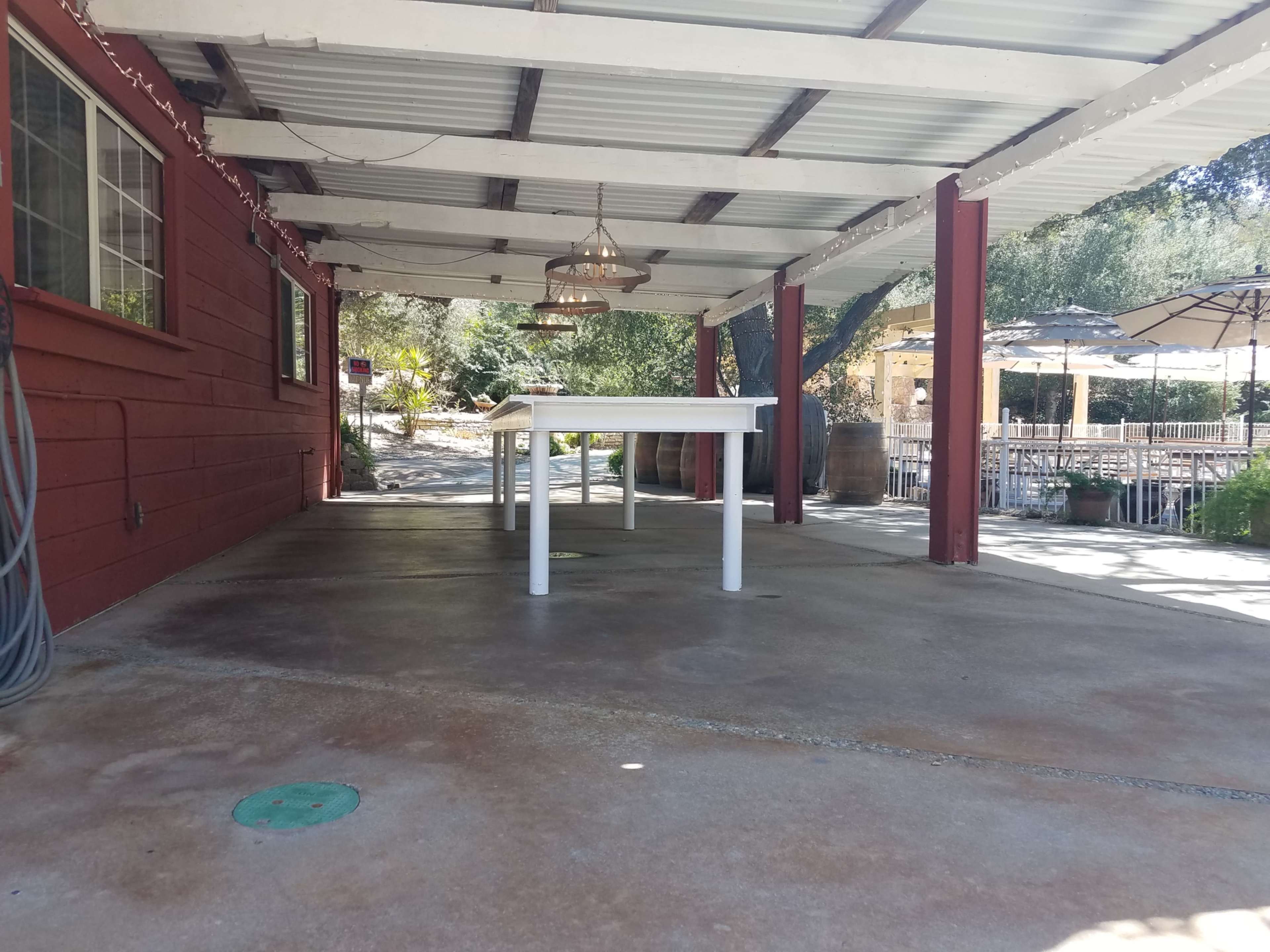 A covered outdoor patio with a white table in the center, surrounded by a concrete floor and red wooden walls.