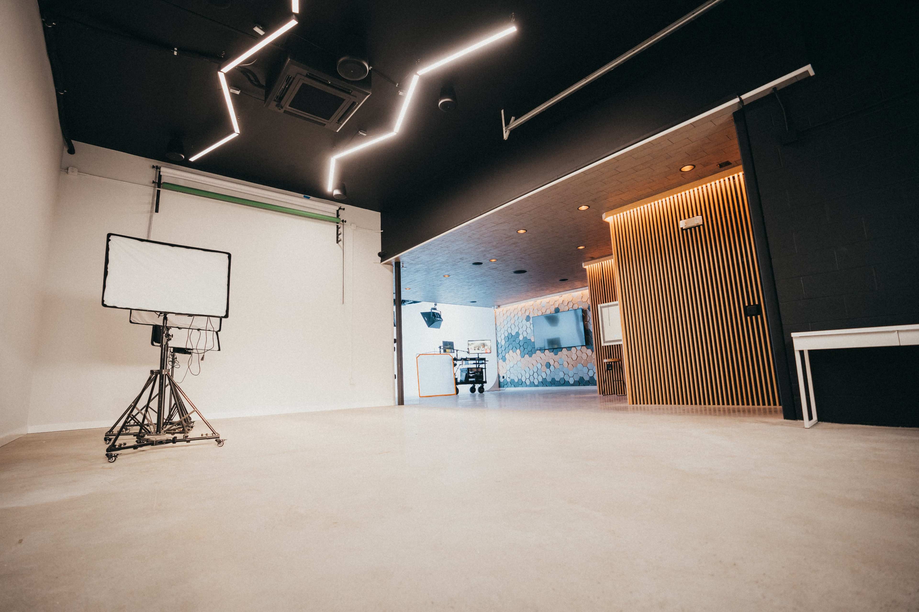 A spacious, modern studio with a lighting setup on wheels, a black wall, and a wooden panel entrance to another area decorated with abstract designs.