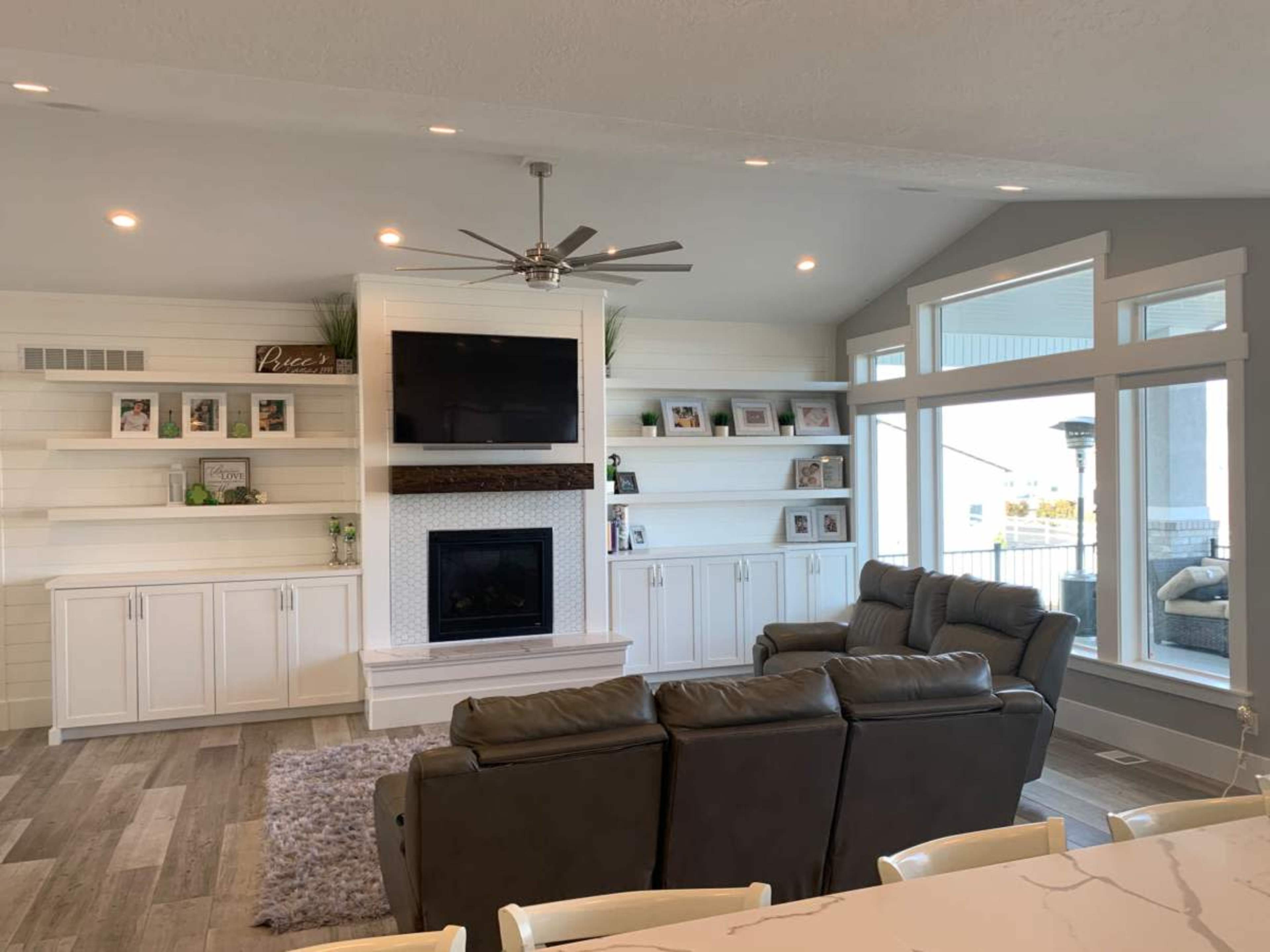 The image shows a modern living room with a fireplace, a mounted television, and large windows providing natural light.