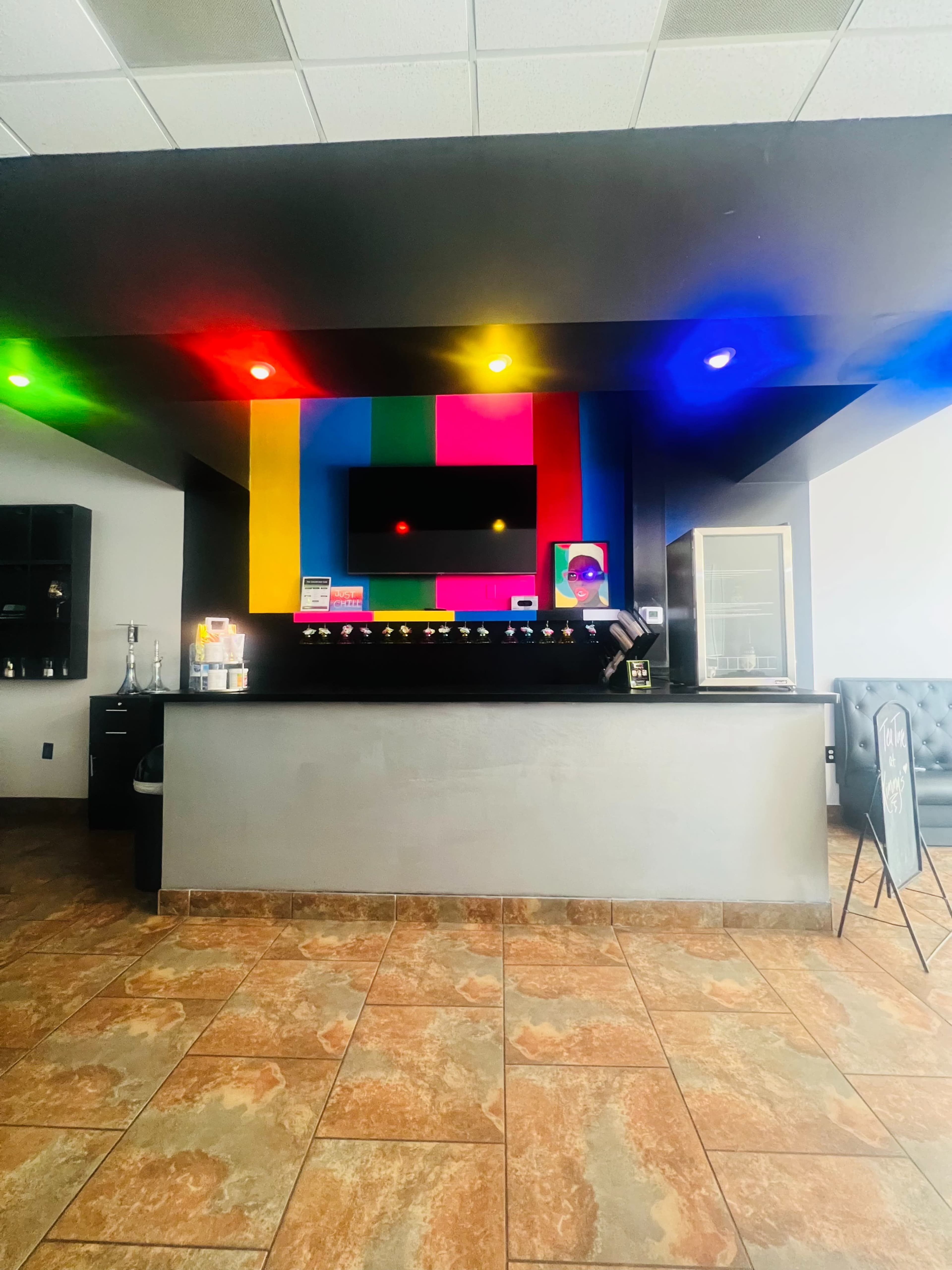A colorful reception area features a black counter and a vivid, framed display with multi-colored lights overhead.