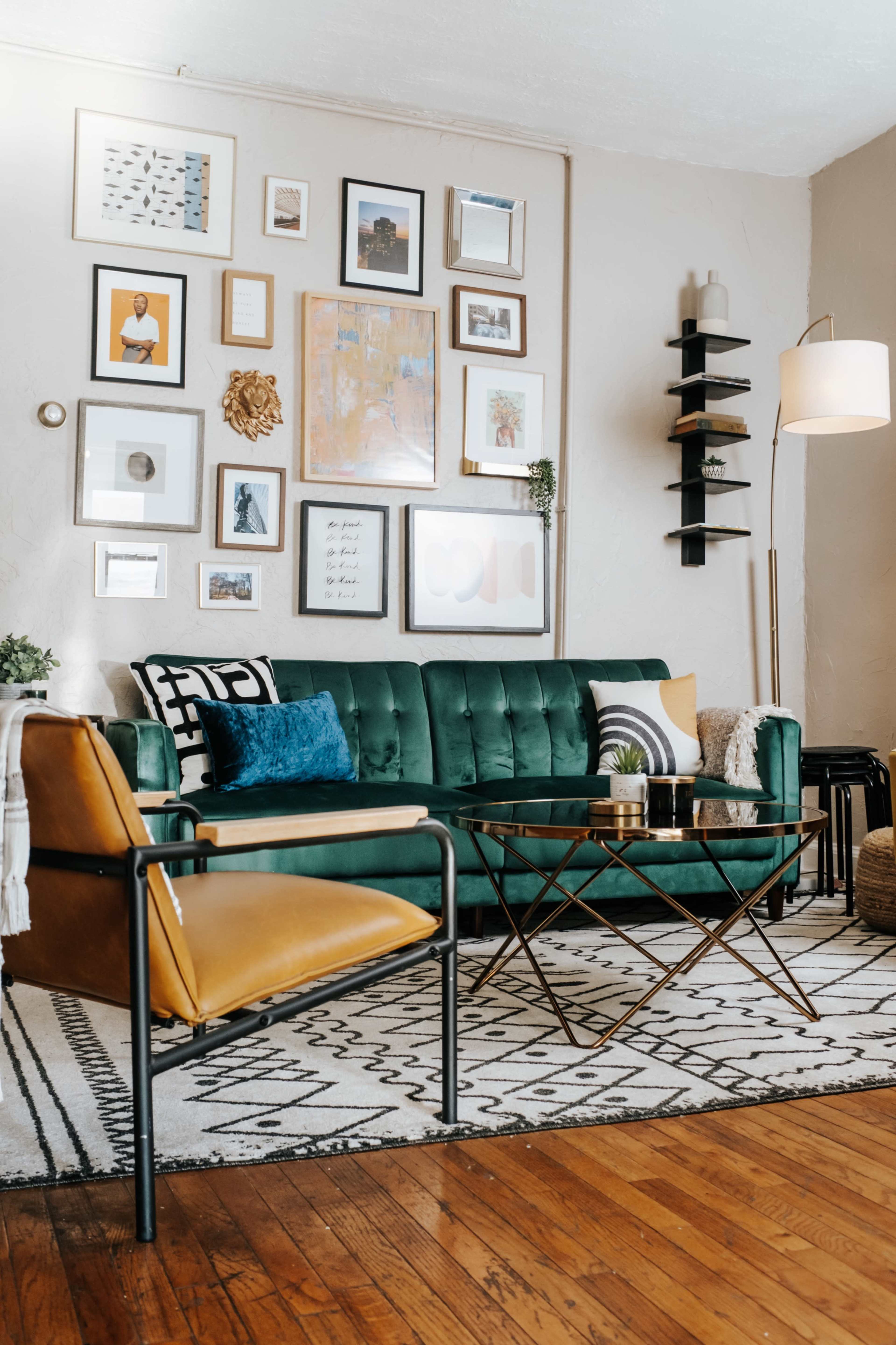 The image depicts a stylish living room featuring a green velvet sofa, a gallery wall of framed art, and a coffee table set on a patterned rug.