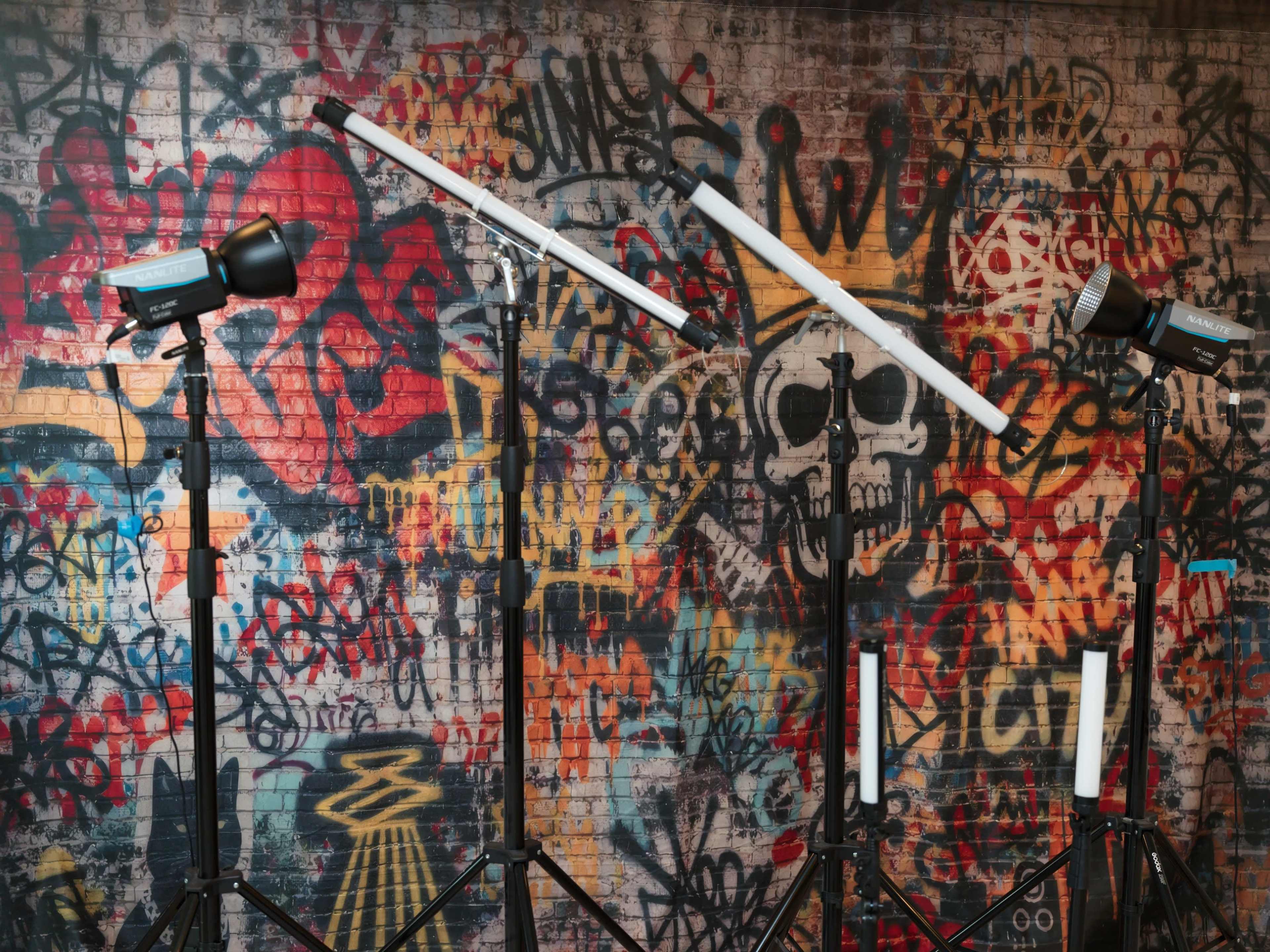 The image shows photography lighting equipment set up in front of a graffiti-covered wall featuring a skull design.