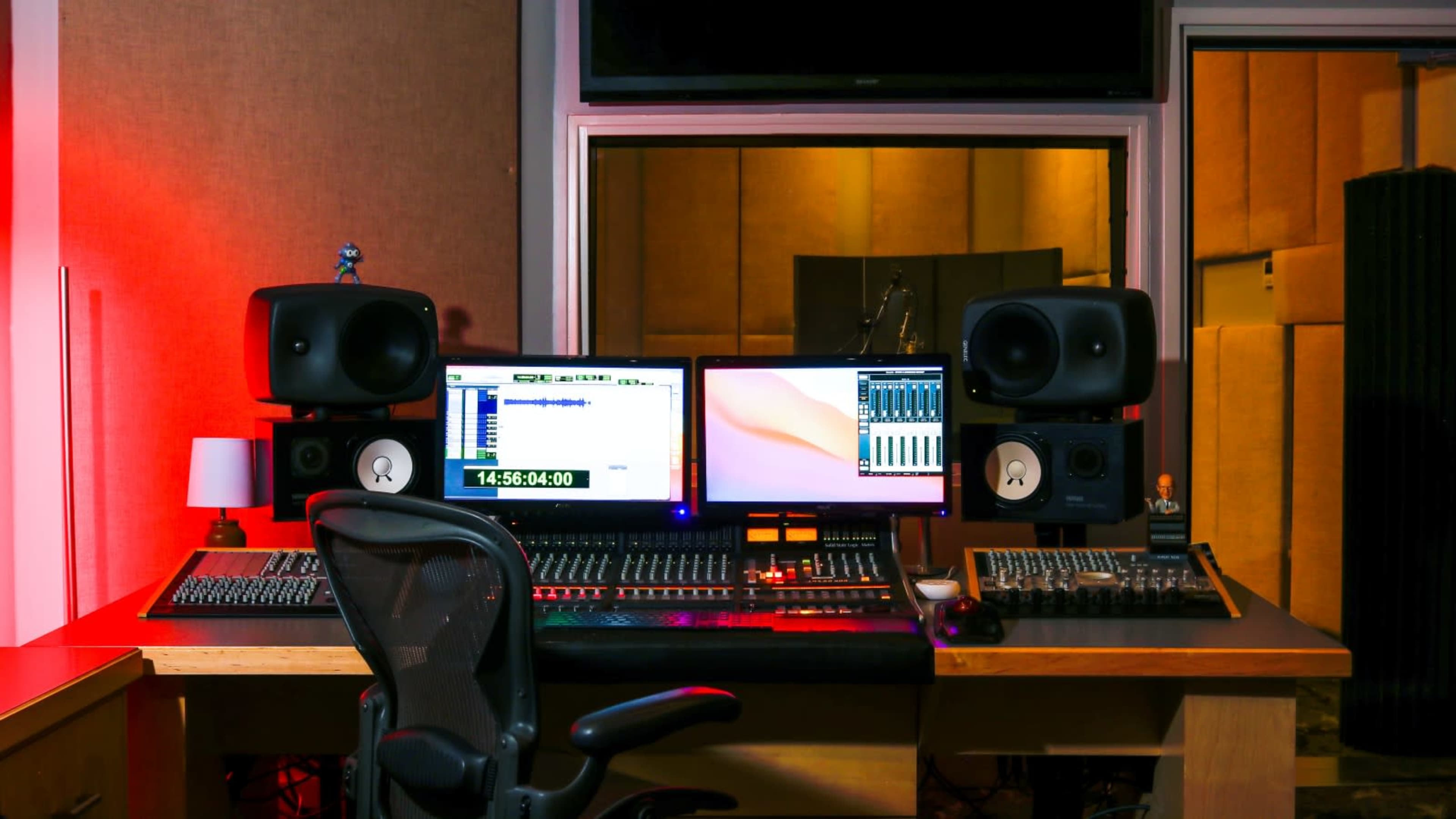 The image shows a music production studio featuring a desk with dual computer monitors, audio mixing equipment, and studio speakers.