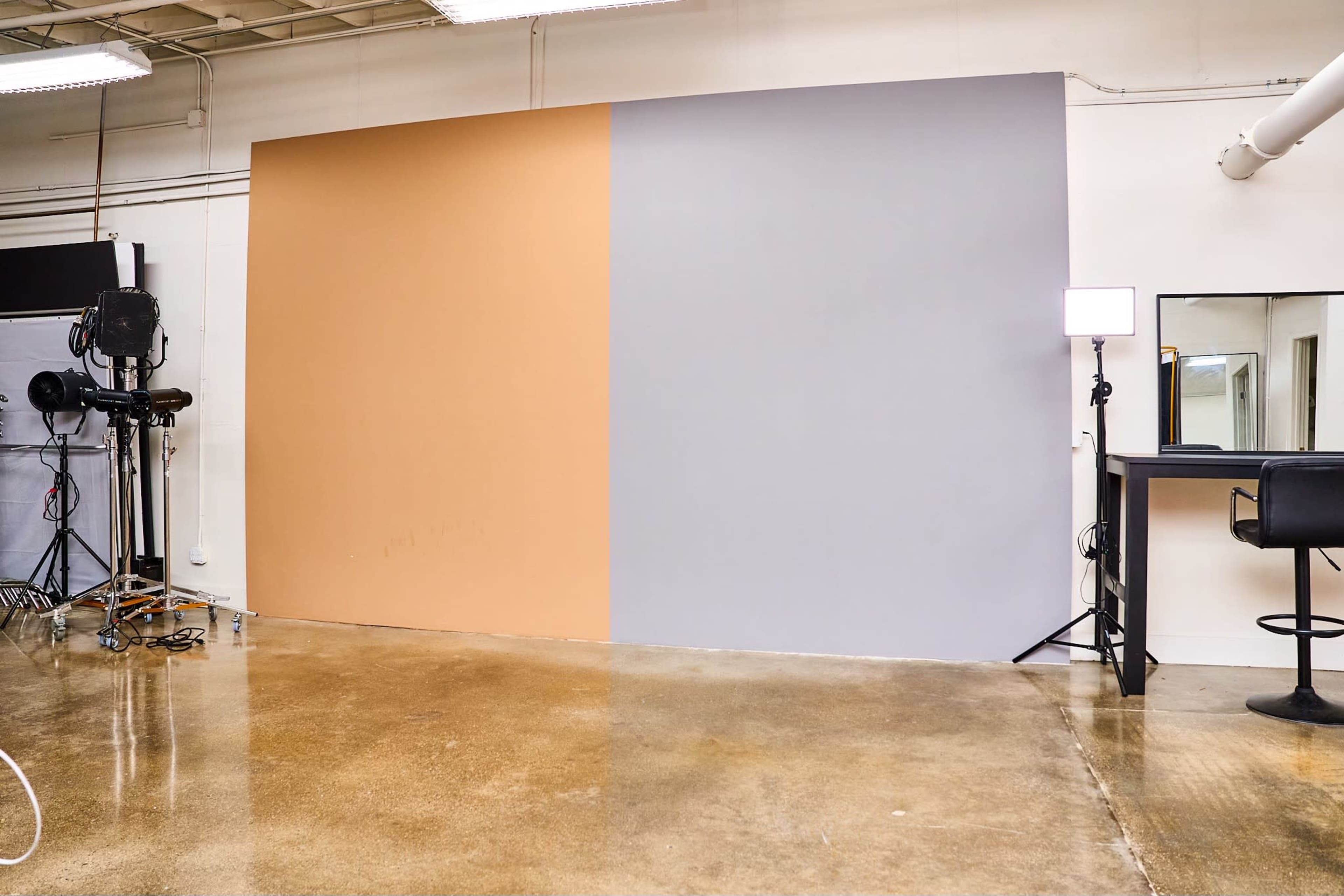 A studio space with a divided wall featuring one half painted in a light brown color and the other half in light gray, accompanied by a black chair and a light setup on the side.