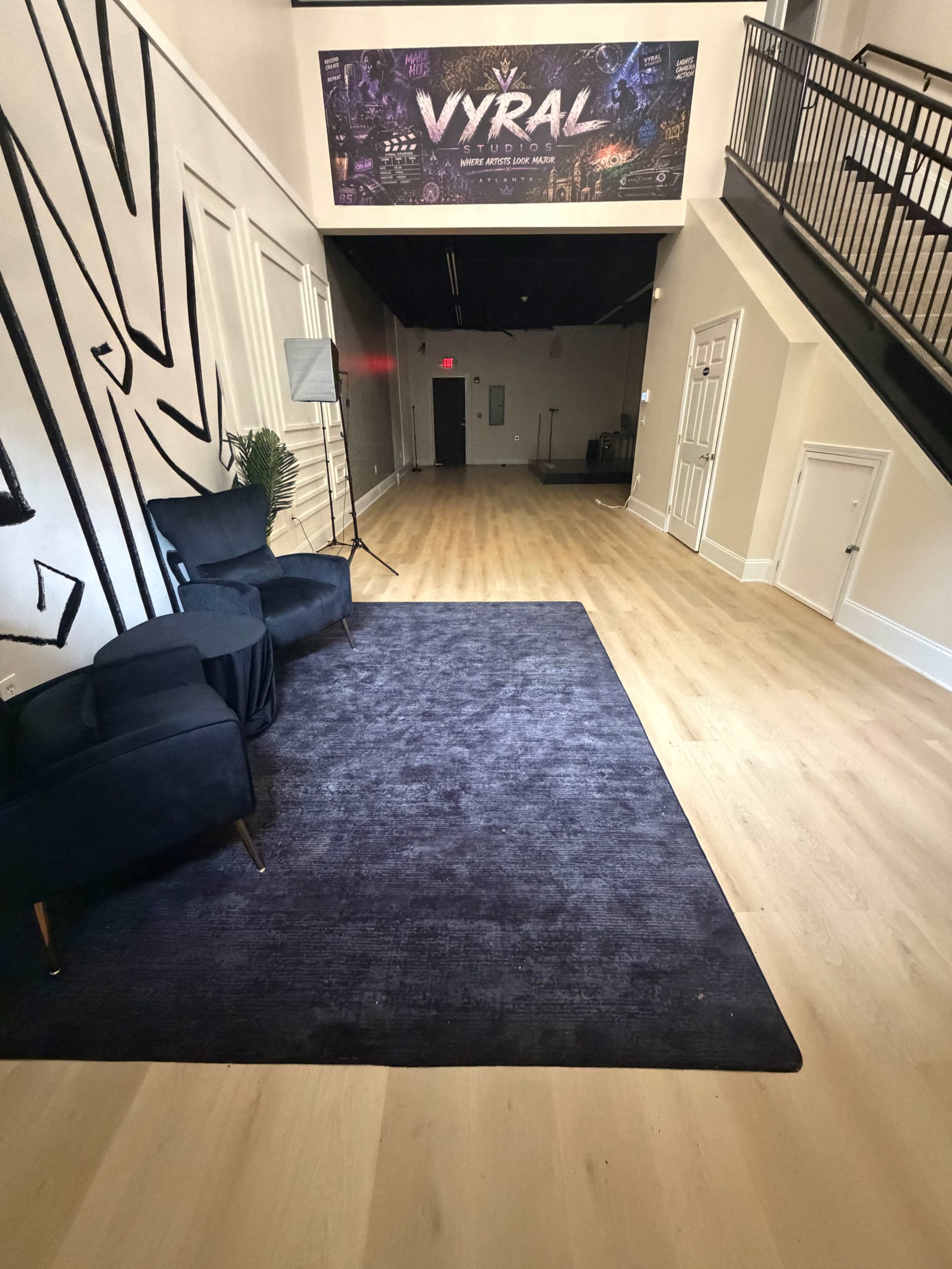 The image shows a spacious hallway featuring a dark rug, two blue chairs, and a large banner on the wall with the word "VYRAL."