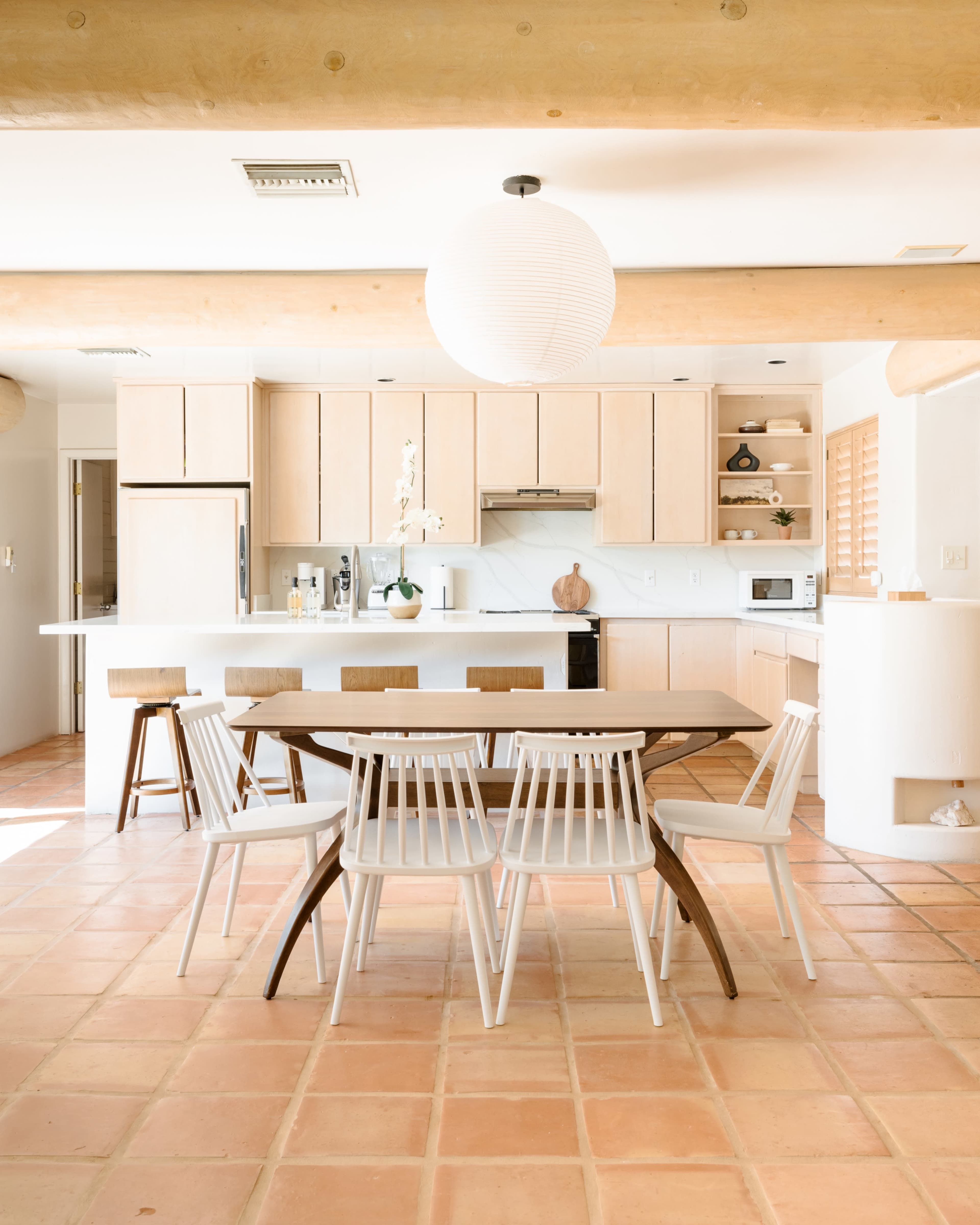 A modern kitchen features light wood cabinetry, a round wooden dining table surrounded by white chairs, and a pendant light illuminating the space.