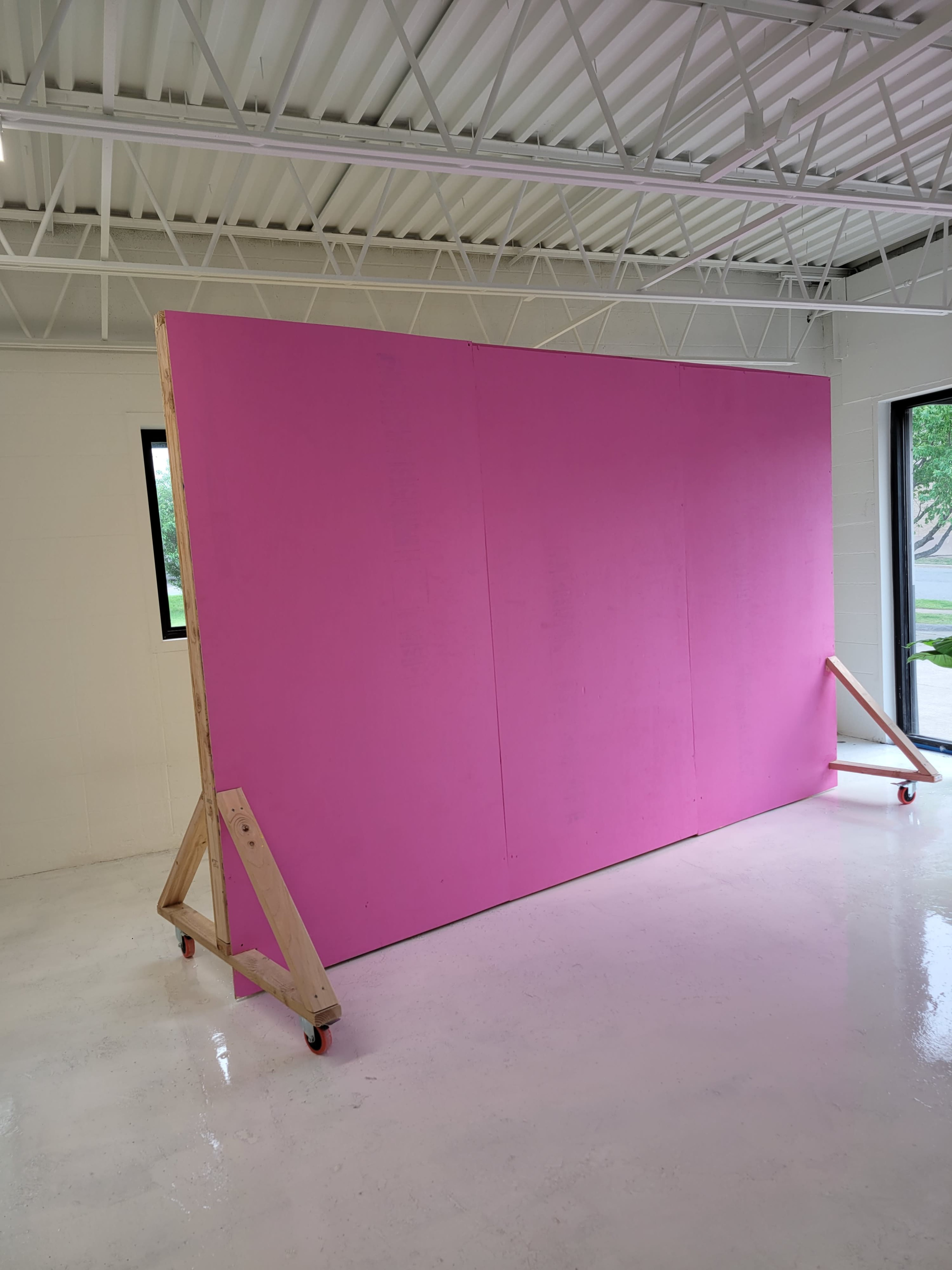 A large pink board is propped up on wooden supports with wheels in a brightly lit indoor space.