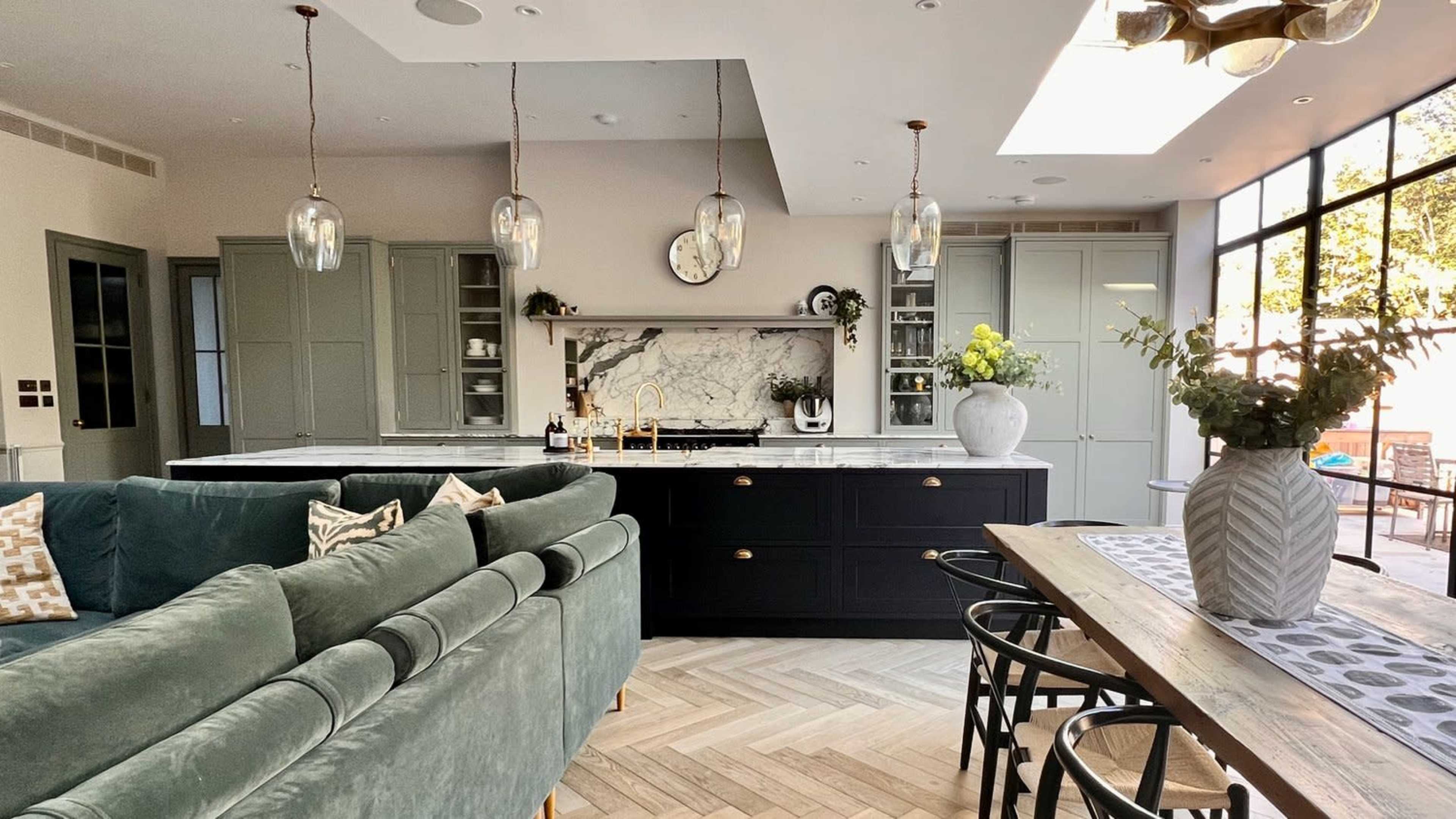 A modern kitchen and dining area featuring a large island with a marble countertop, black cabinetry, and ample natural light from expansive windows.