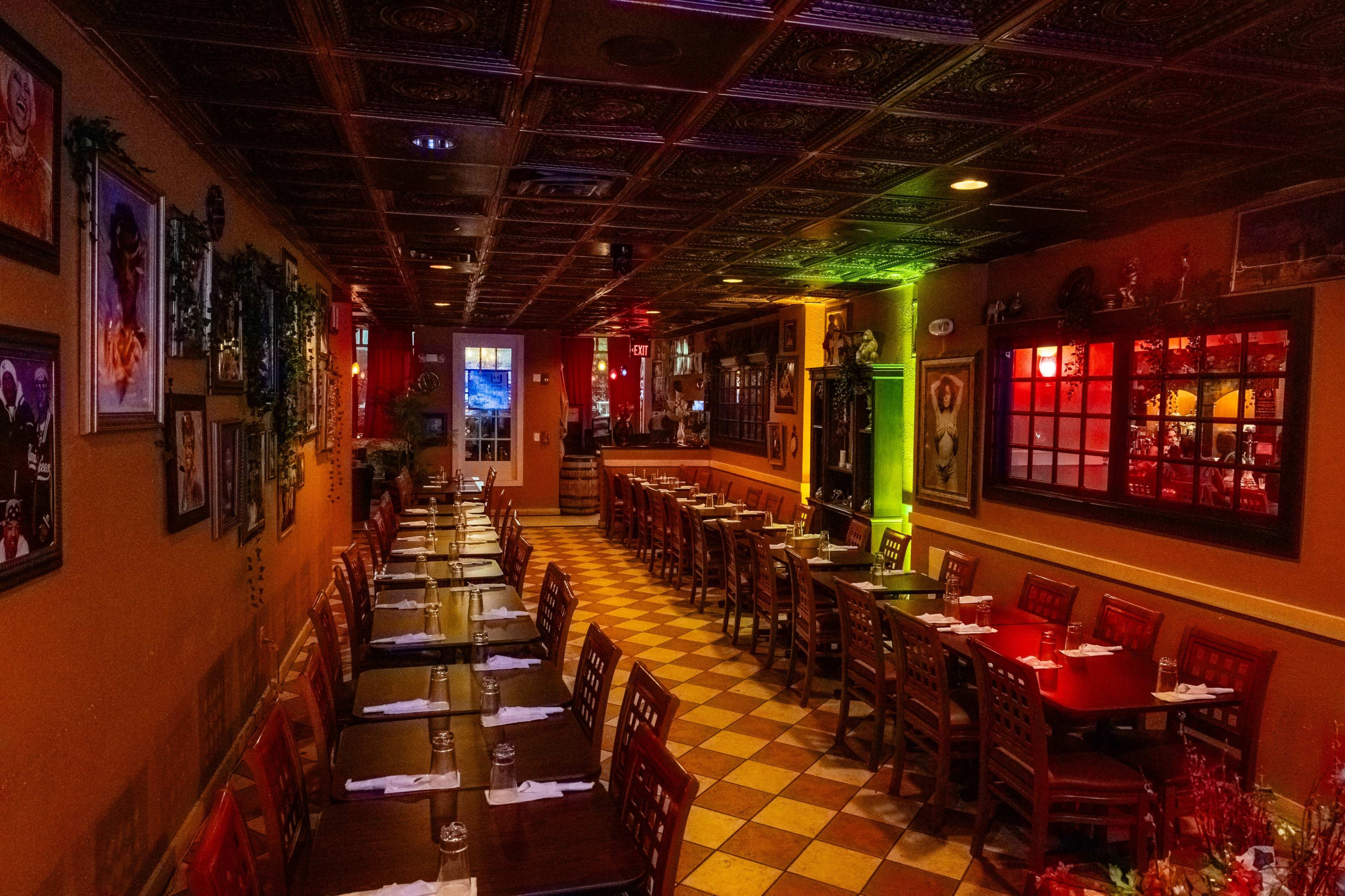 A long, neatly arranged dining area in a restaurant features wooden tables and chairs, with decorative wall art and colorful lighting.
