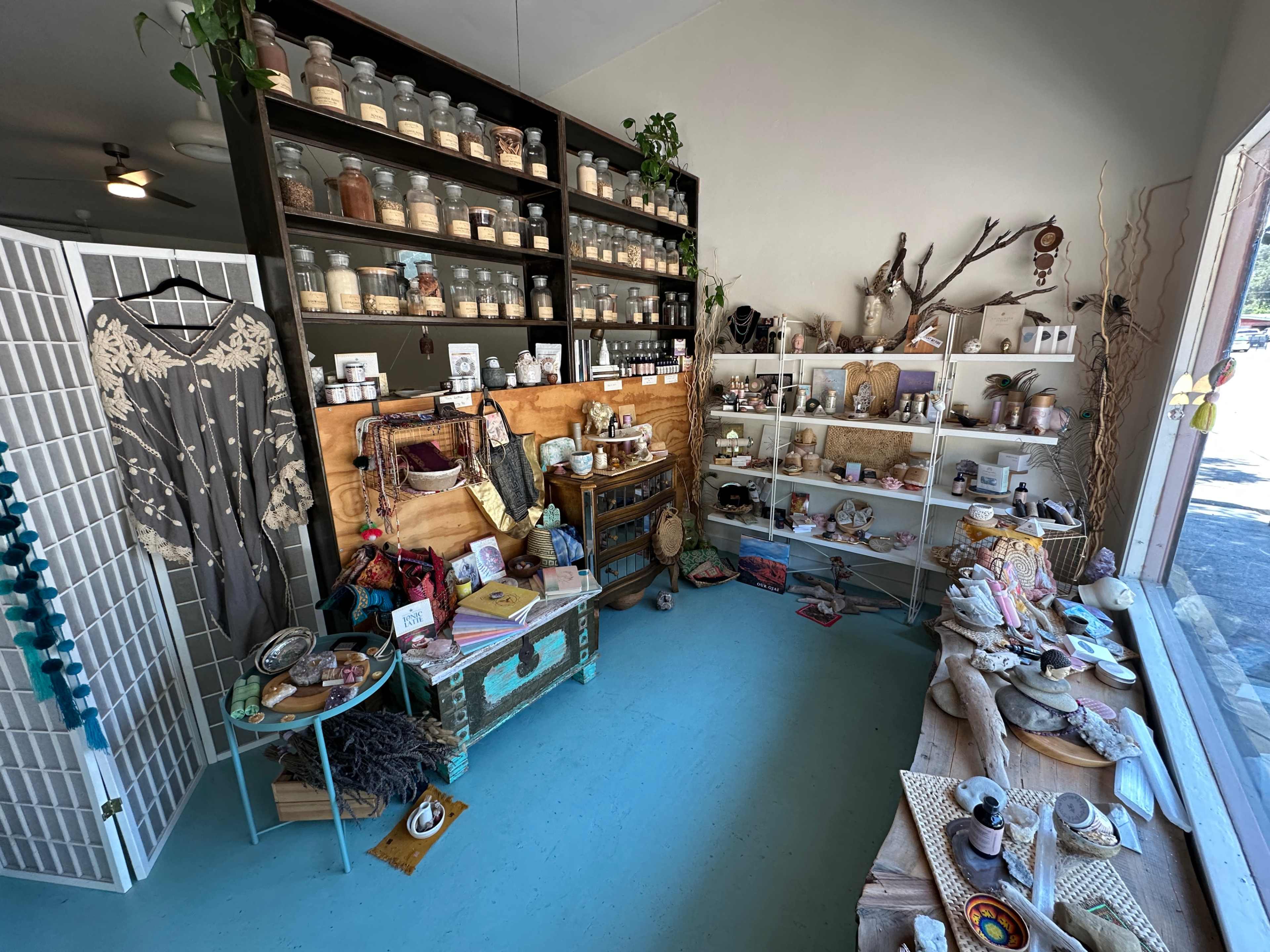 The image shows a cozy boutique interior filled with various decorative items, jars, and handmade goods displayed on shelves and tables.